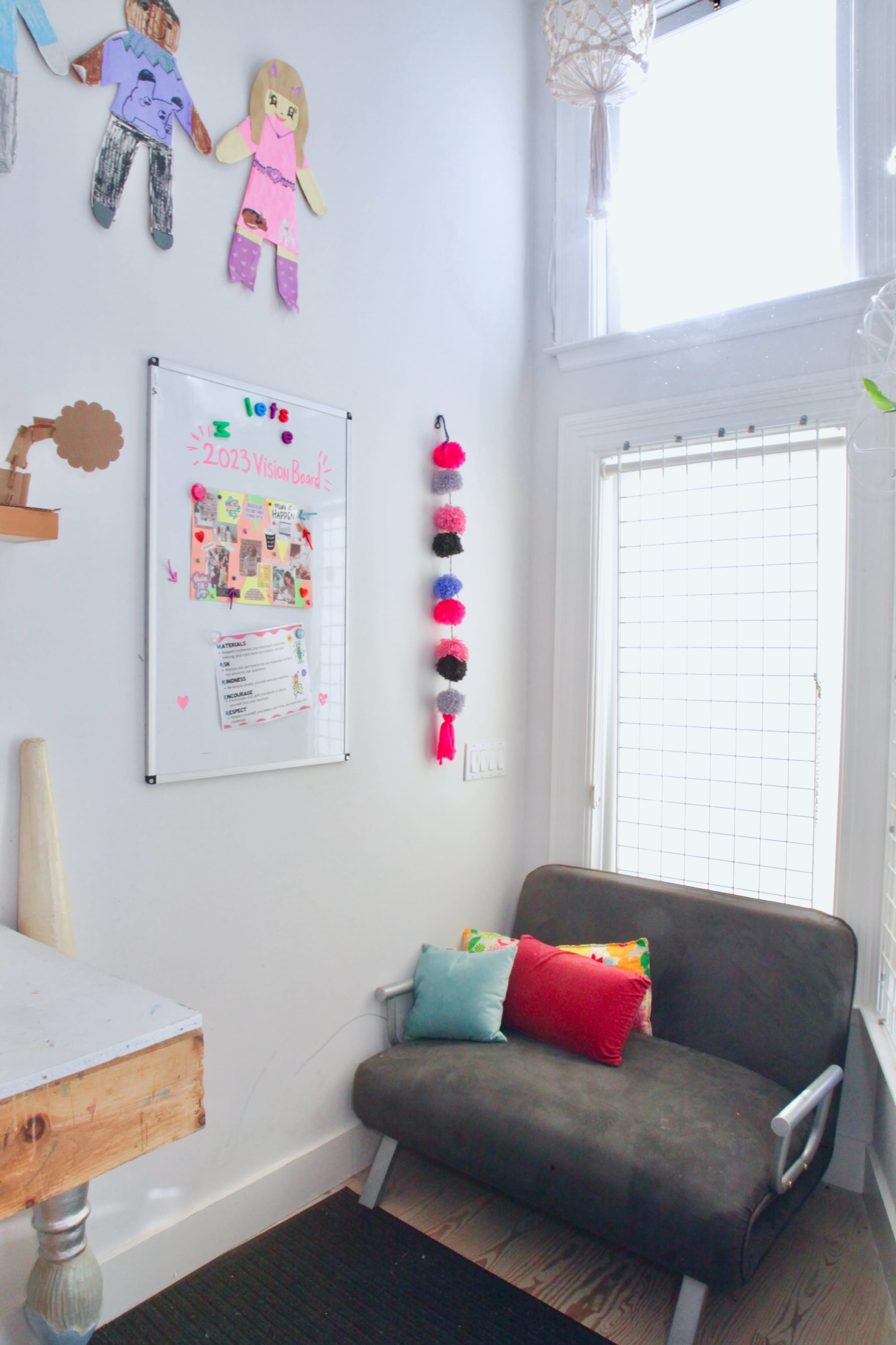 A small sitting area with a gray couch, colorful cushions, and children's artwork displayed on the walls.