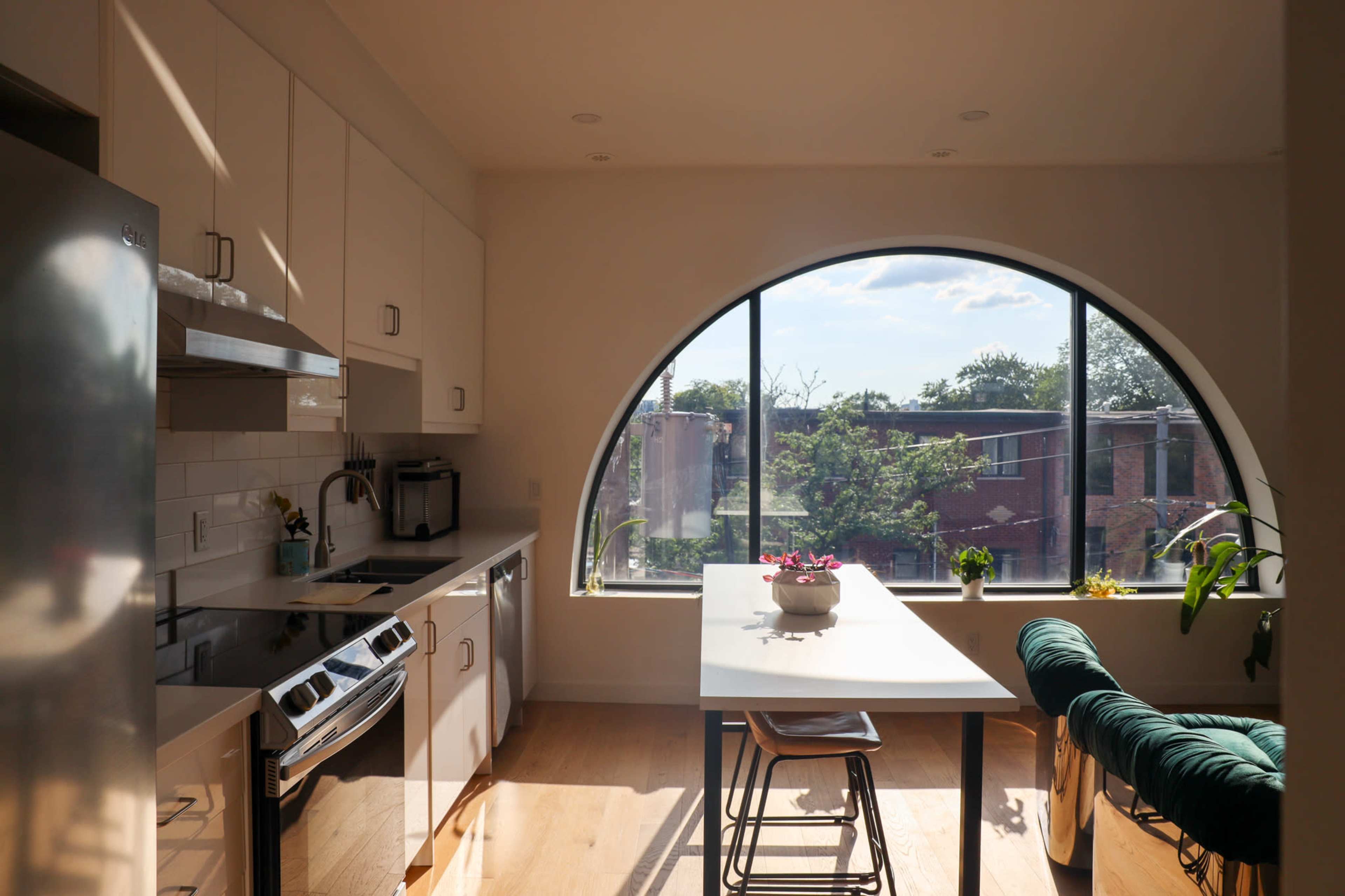 A modern kitchen features a bright, arched window overlooking a landscaped outdoor area, with a dining table and chairs positioned nearby.