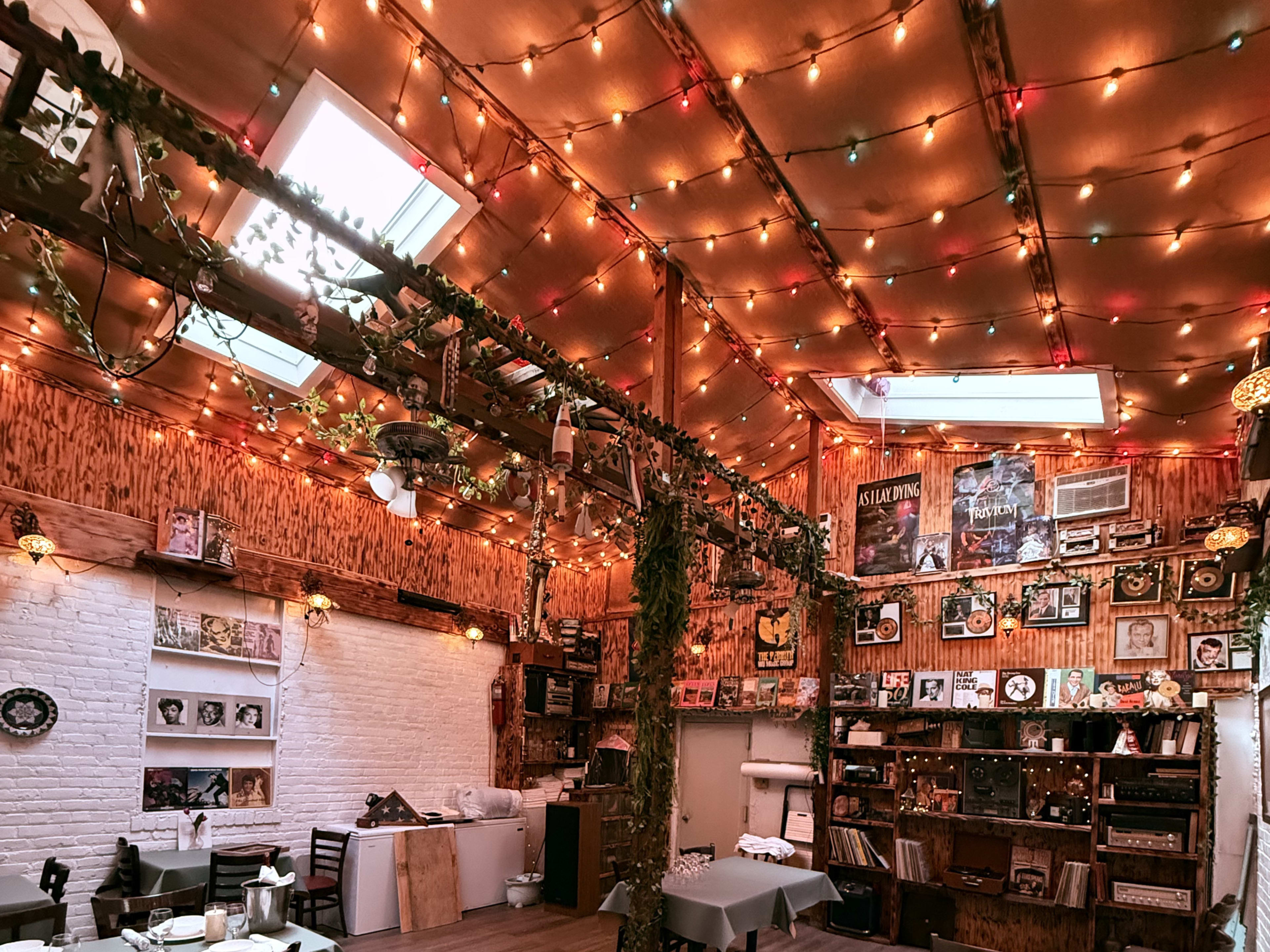 The image depicts a warmly lit cafe interior adorned with fairy lights, wooden beams, and a collection of framed artwork and memorabilia on the walls.