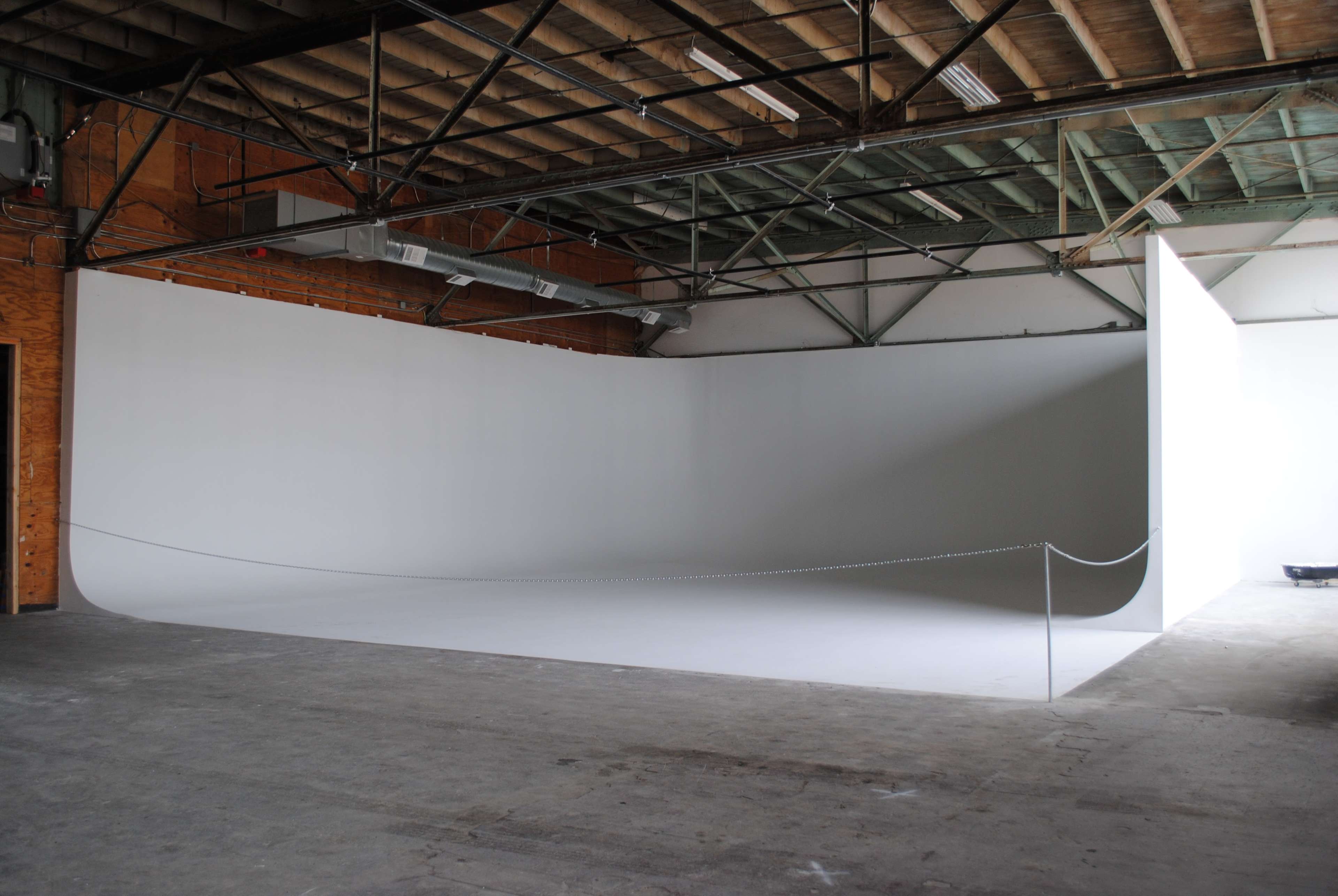 The image shows a spacious studio with a large, curved white backdrop and exposed wooden beams overhead.