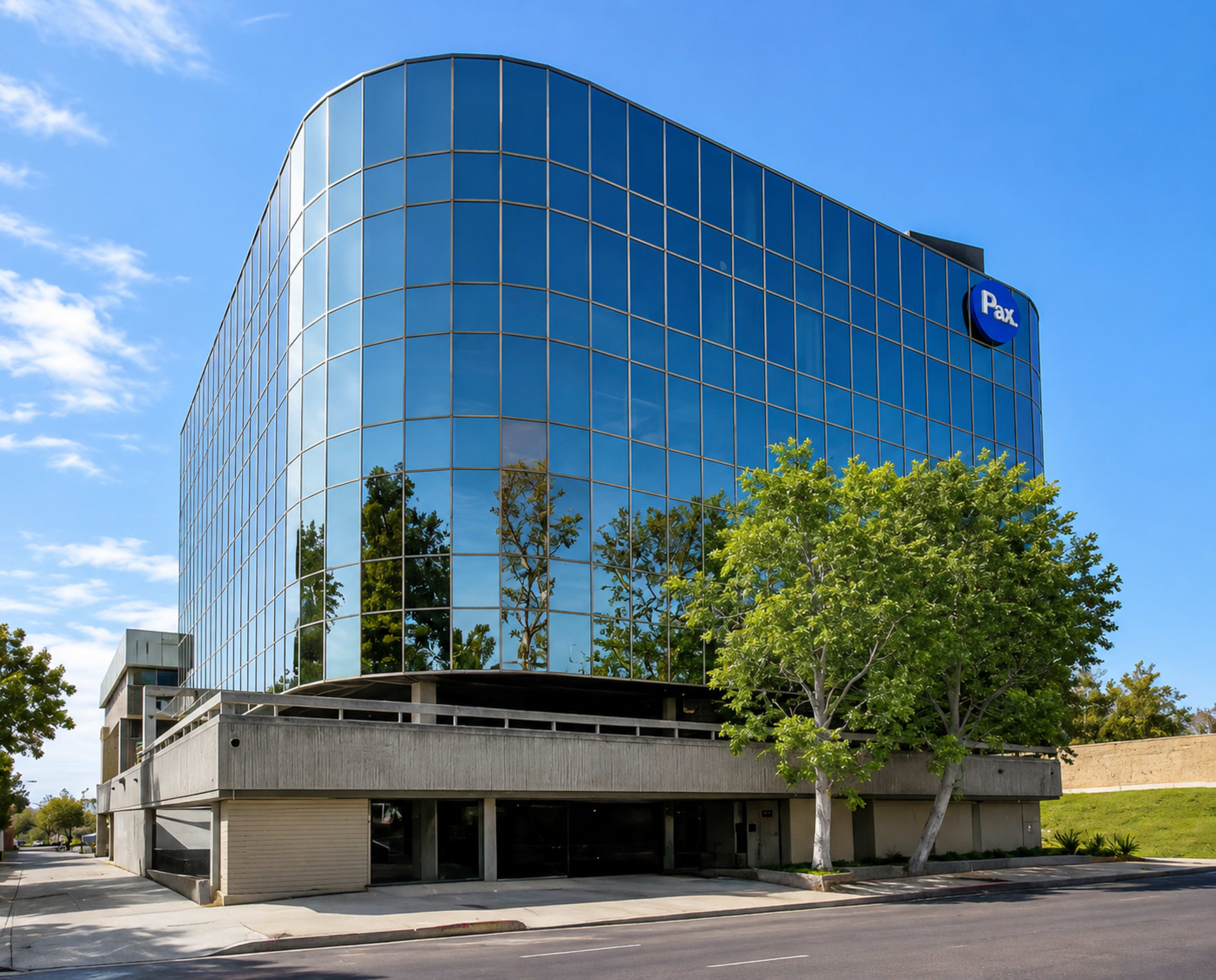 The image shows a modern glass office building with a curved facade and a parking structure at the base, set against a clear blue sky.