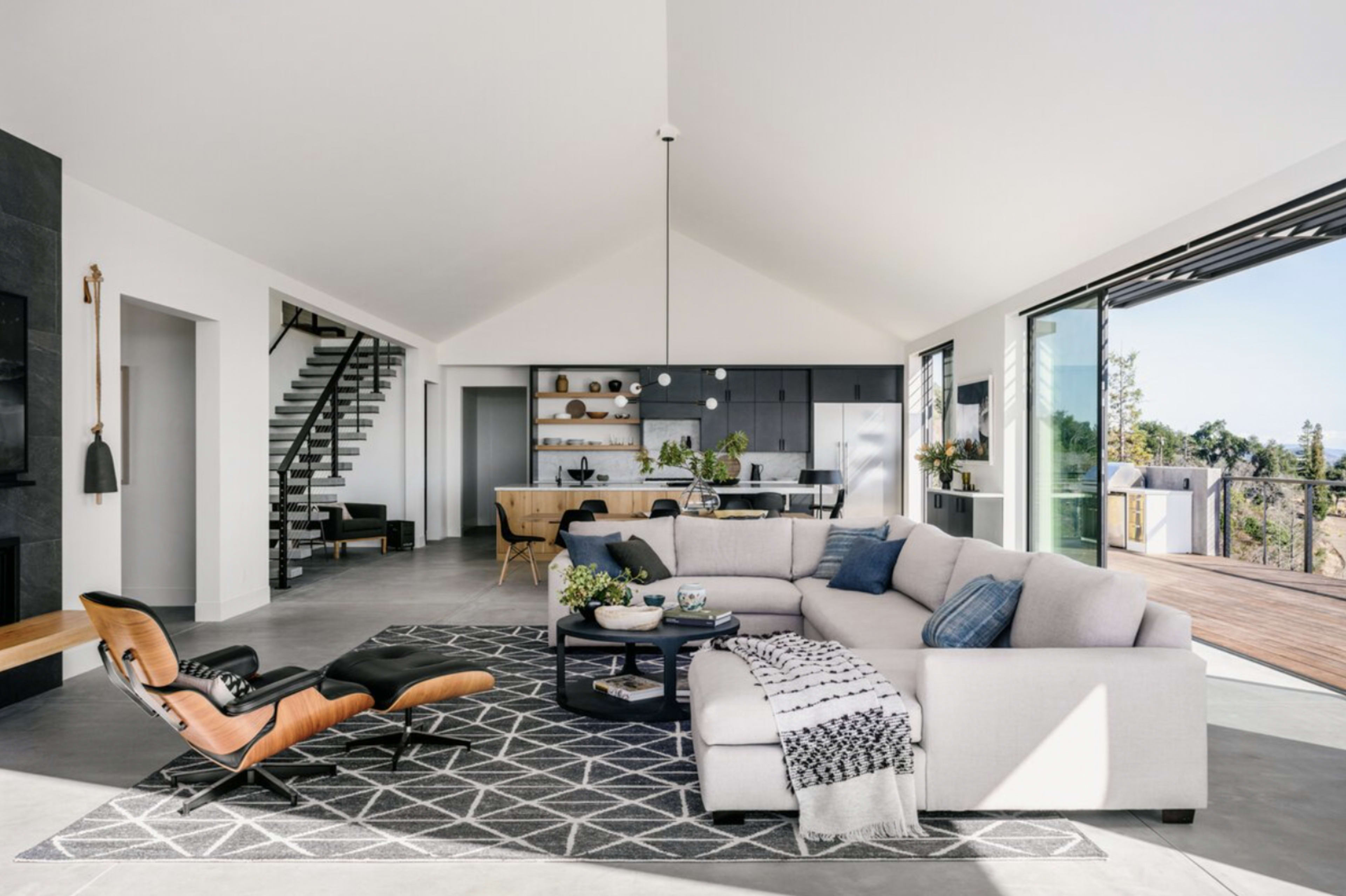 A modern, open-concept living room with a large sectional sofa, a rug, and sliding glass doors leading to an outdoor deck.