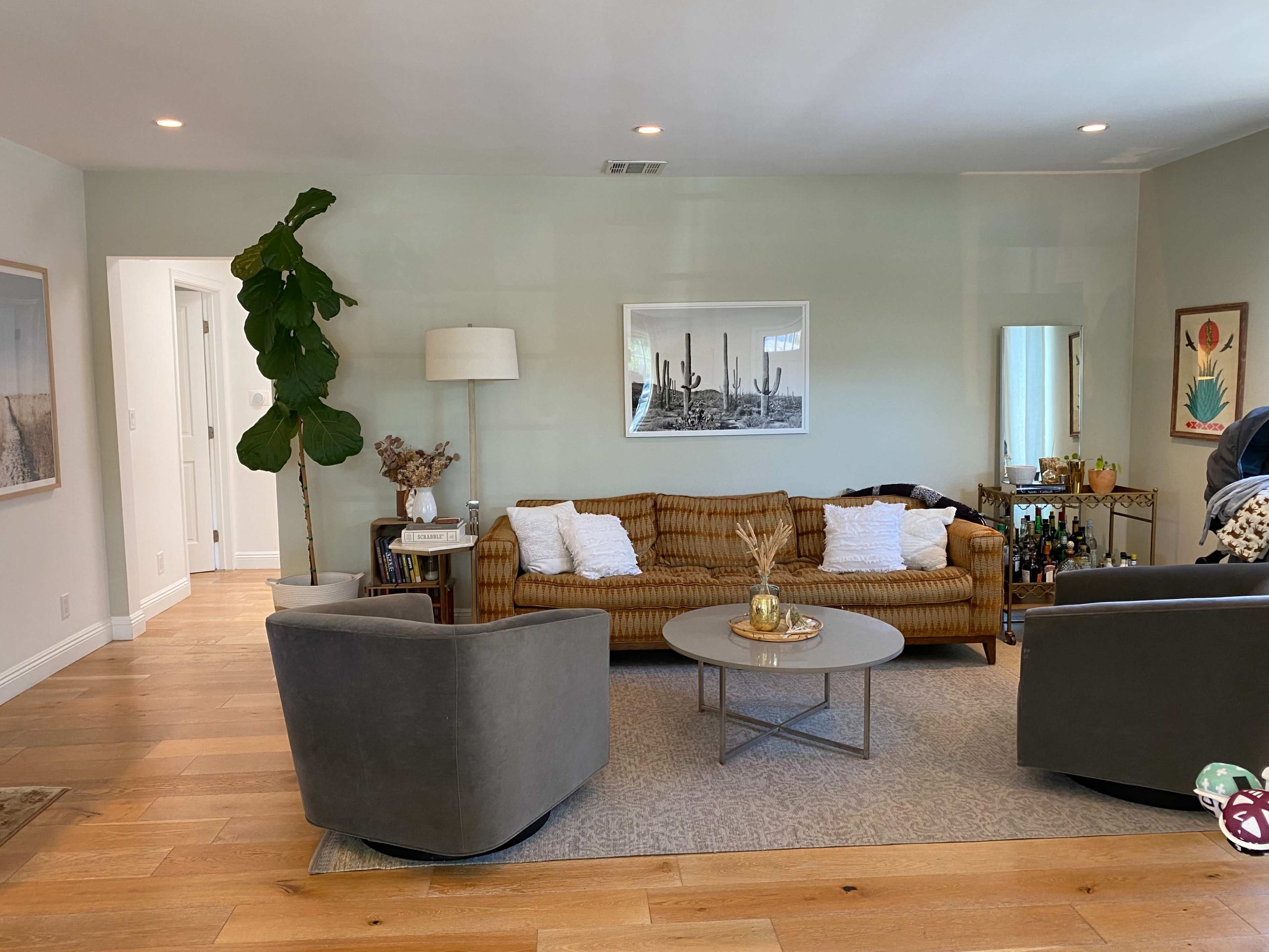 The living room features a brown sofa, two gray armchairs, a circular coffee table, and various decorative elements against a light green wall.