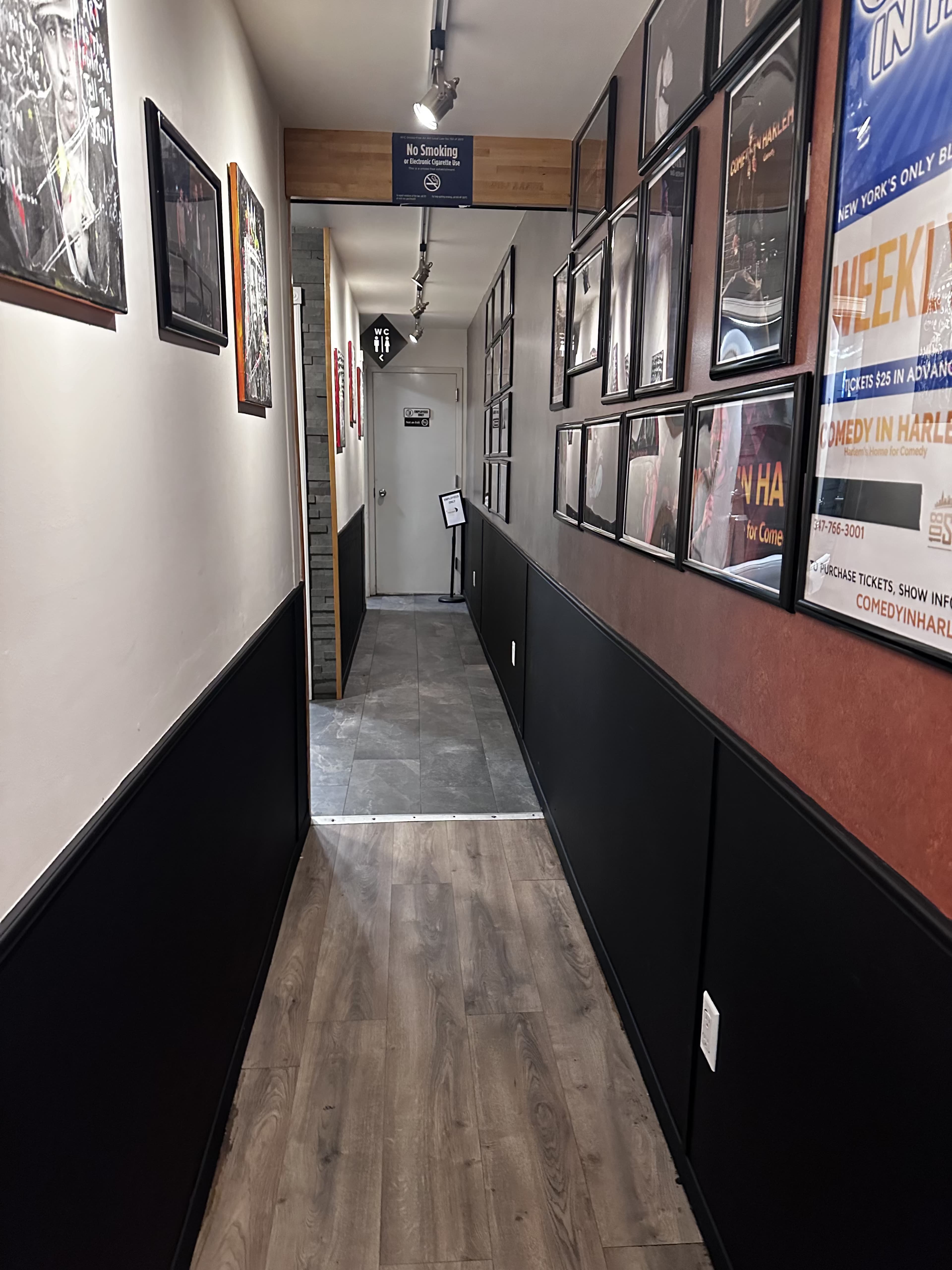 A narrow hallway lined with framed pictures leads to an exit marked with a "No Smoking" sign.