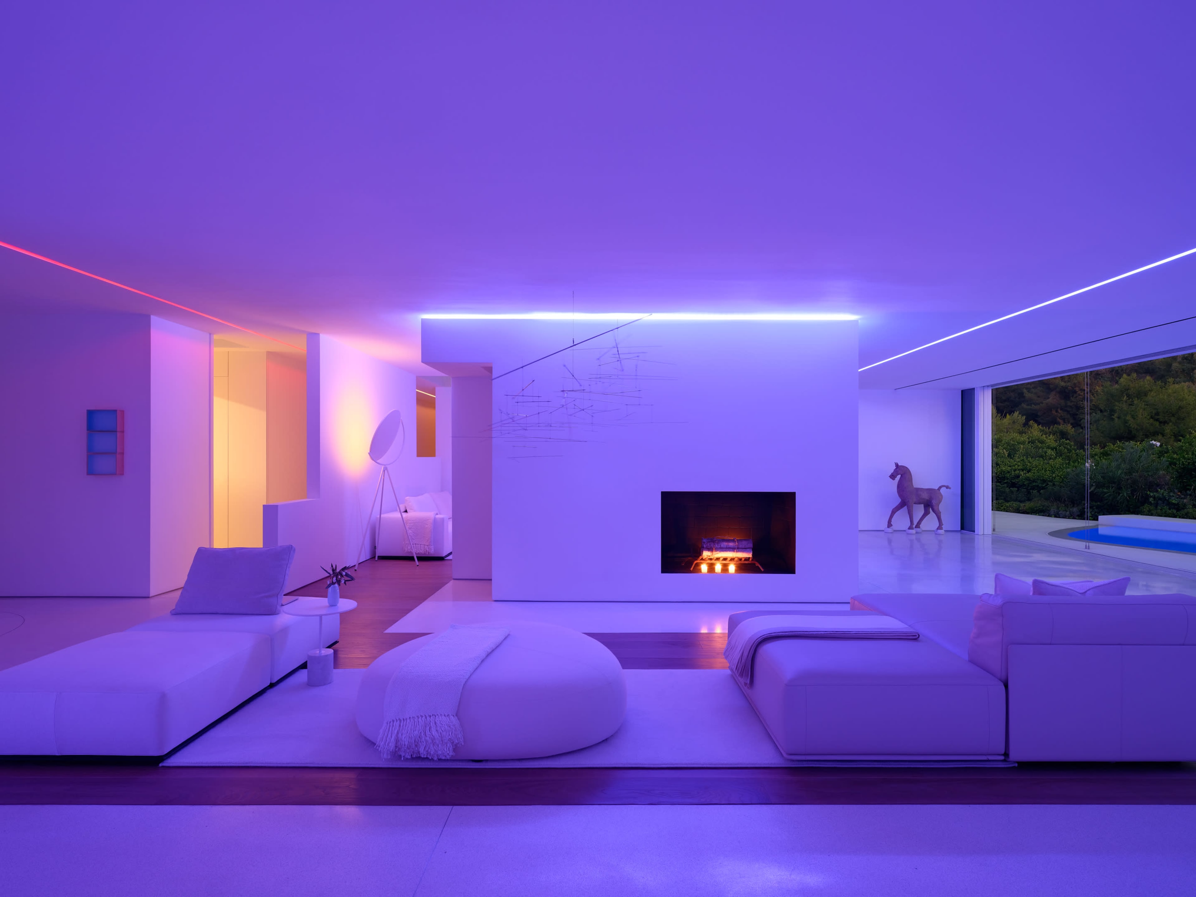 The image shows a modern living room with minimalist furniture, a fireplace, and ambient purple lighting.