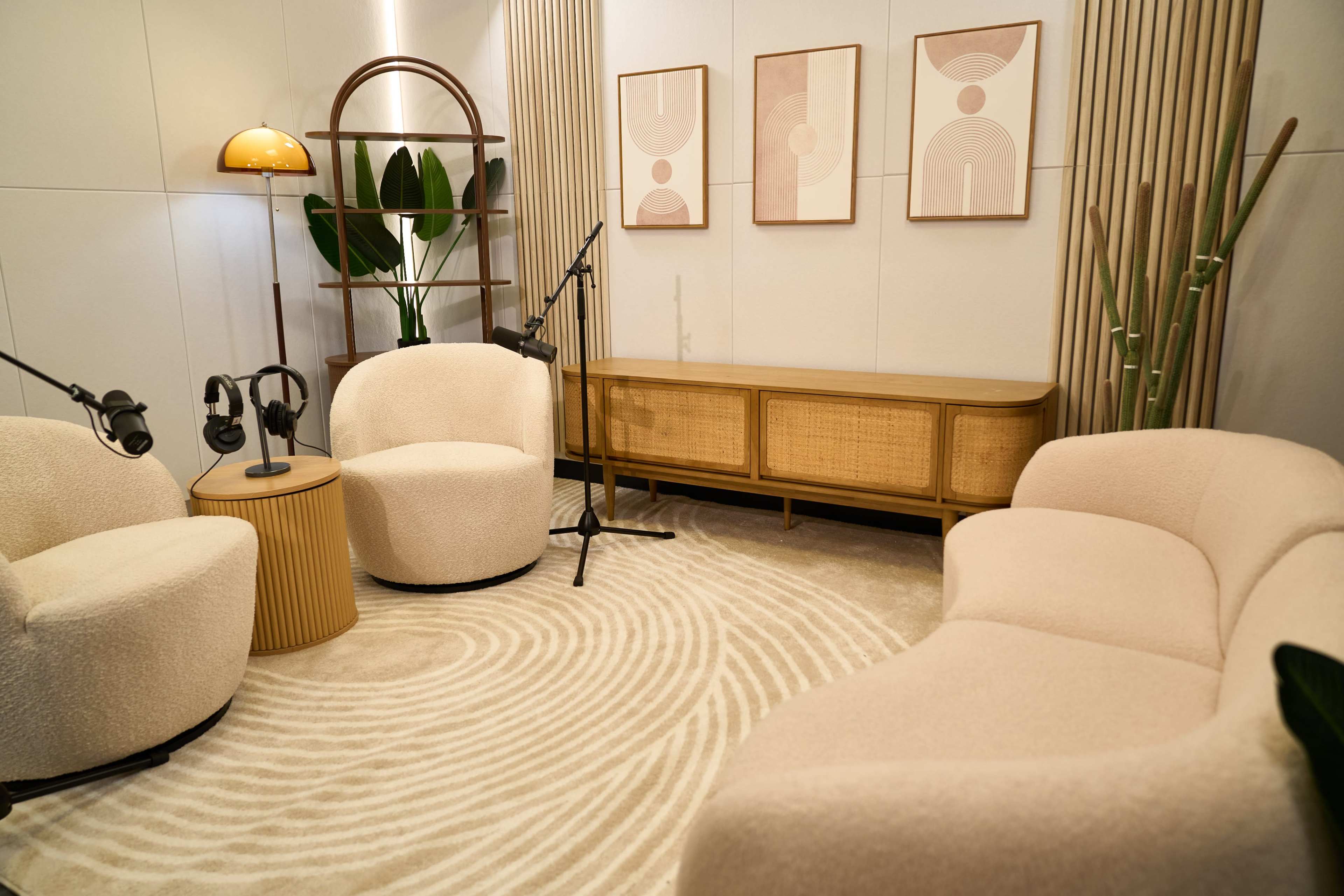 The image shows a cozy, modern seating area featuring two plush armchairs, a round side table, a low sofa, and a cabinet, all arranged on a circular patterned rug.