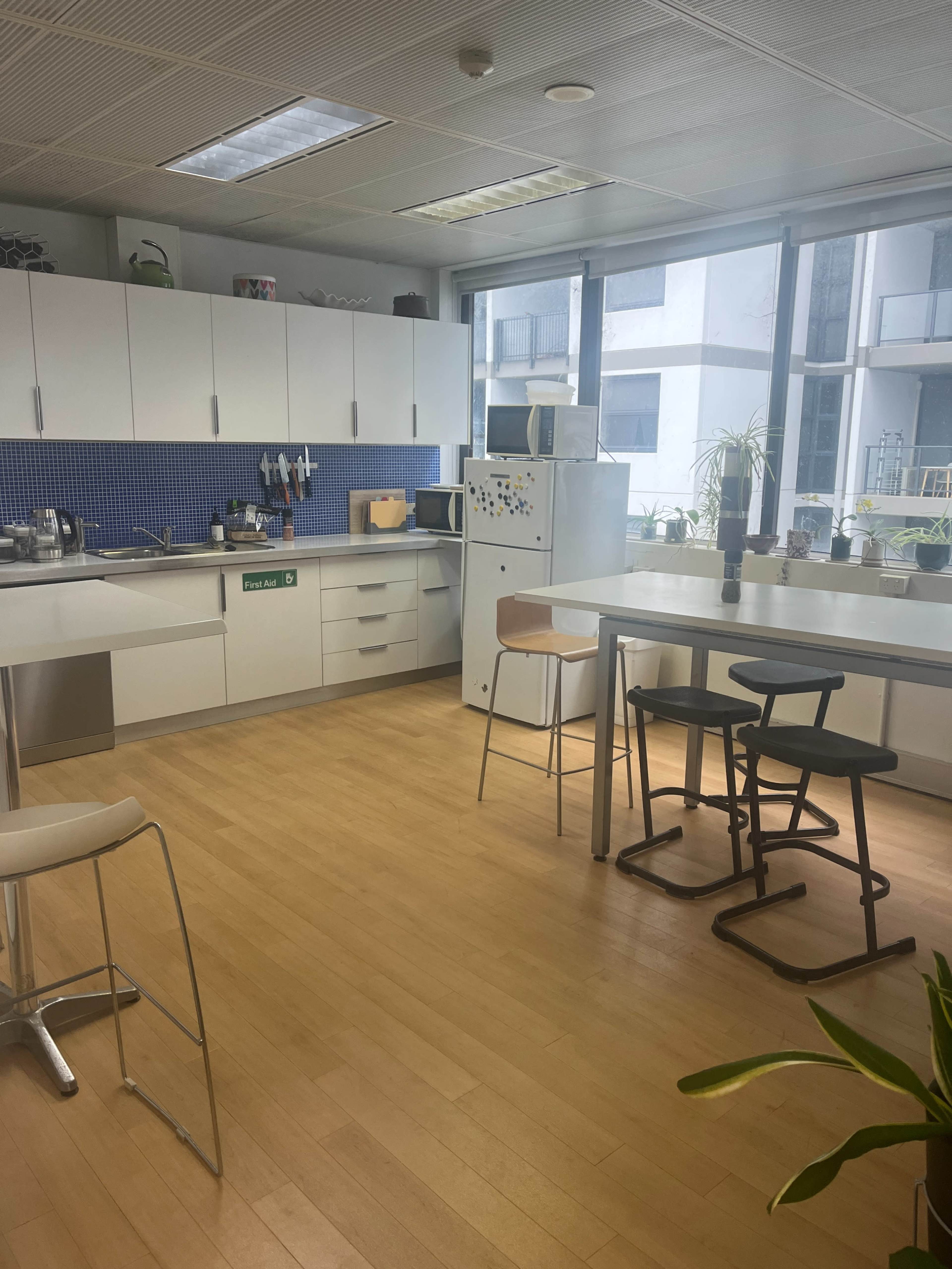 The image shows a modern kitchen area with white cabinets, a blue tiled backsplash, a refrigerator, and a table with chairs.