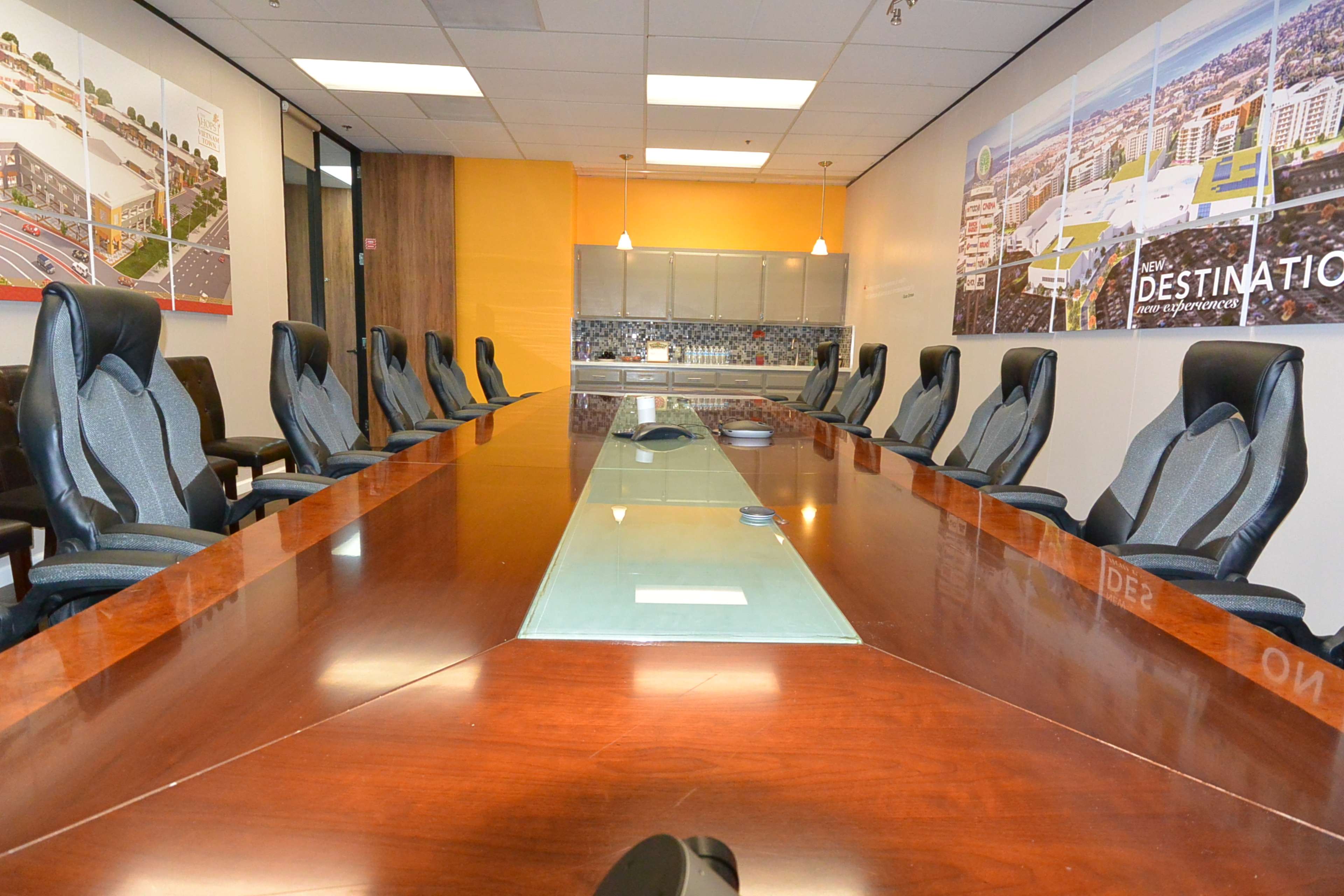 A long conference table with a glass center is surrounded by several high-backed chairs in a modern meeting room.