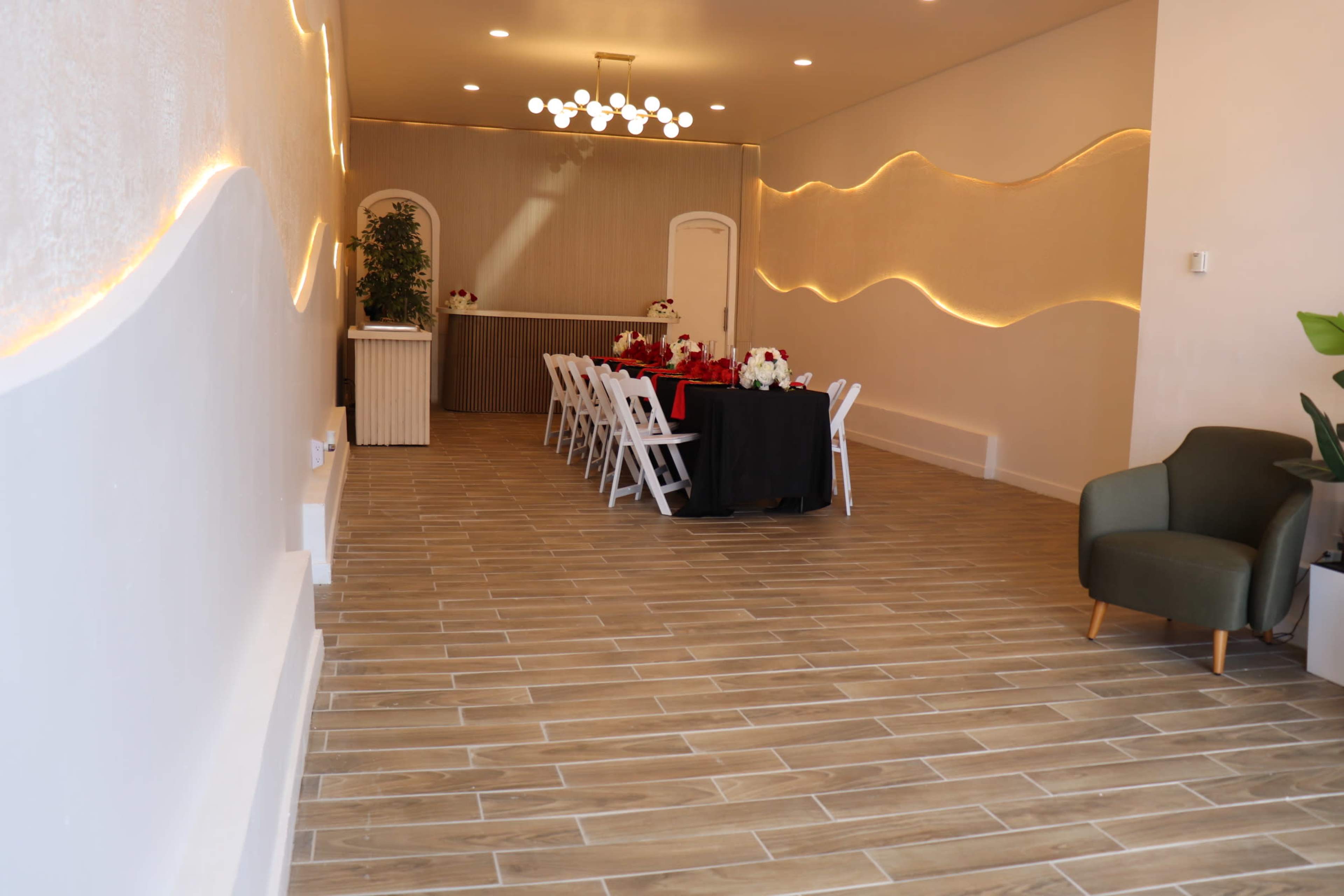 The image shows an elegantly set dining area with a long table adorned with red and white decorations, surrounded by white chairs, and featuring a modern decor on the walls and floor.