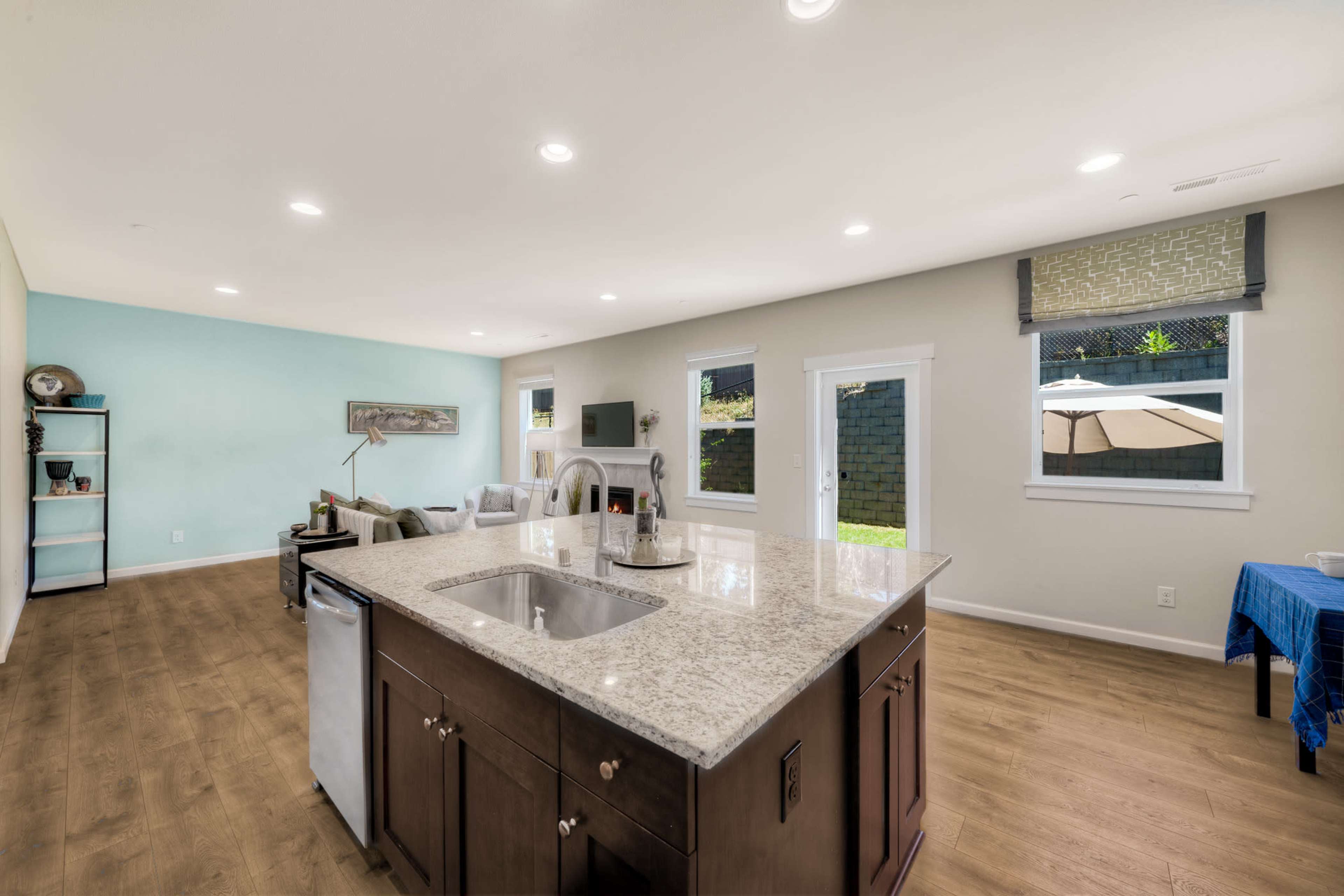 An open-concept kitchen and living area with a granite island, modern appliances, and large windows facing an outdoor space.