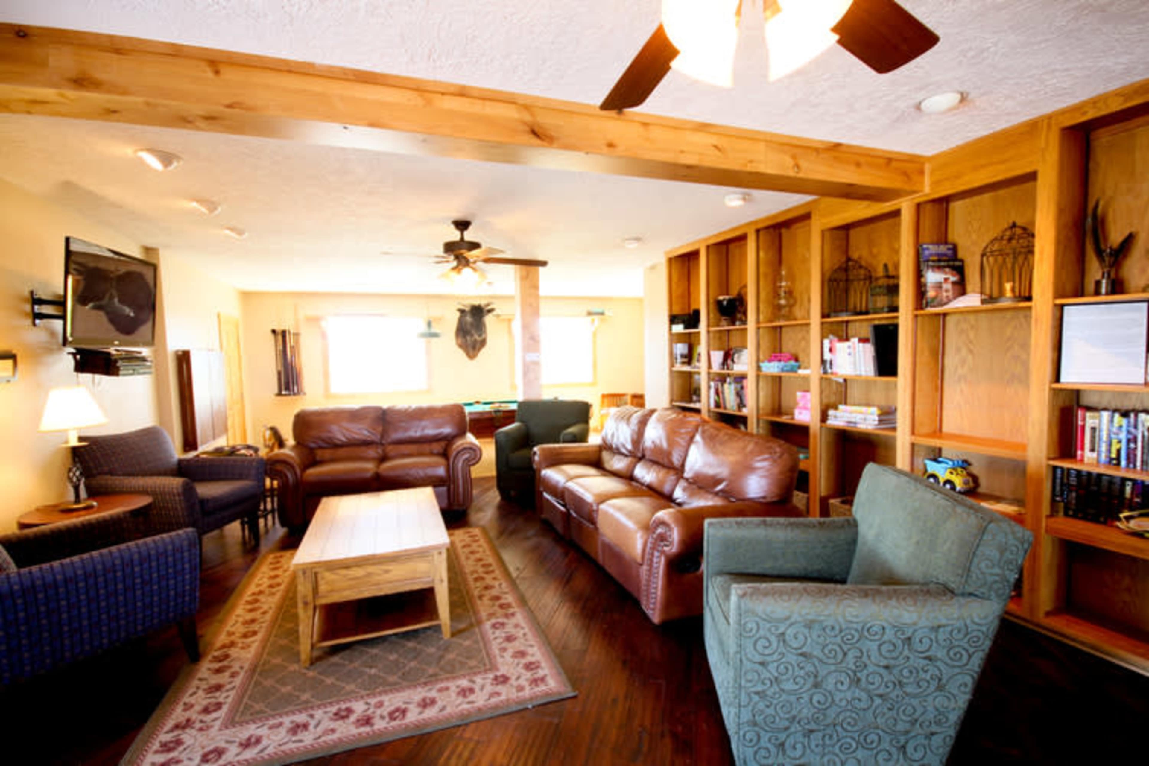 A living room with a mix of leather and upholstered seating, a wooden coffee table, built-in bookshelves, and a ceiling fan.