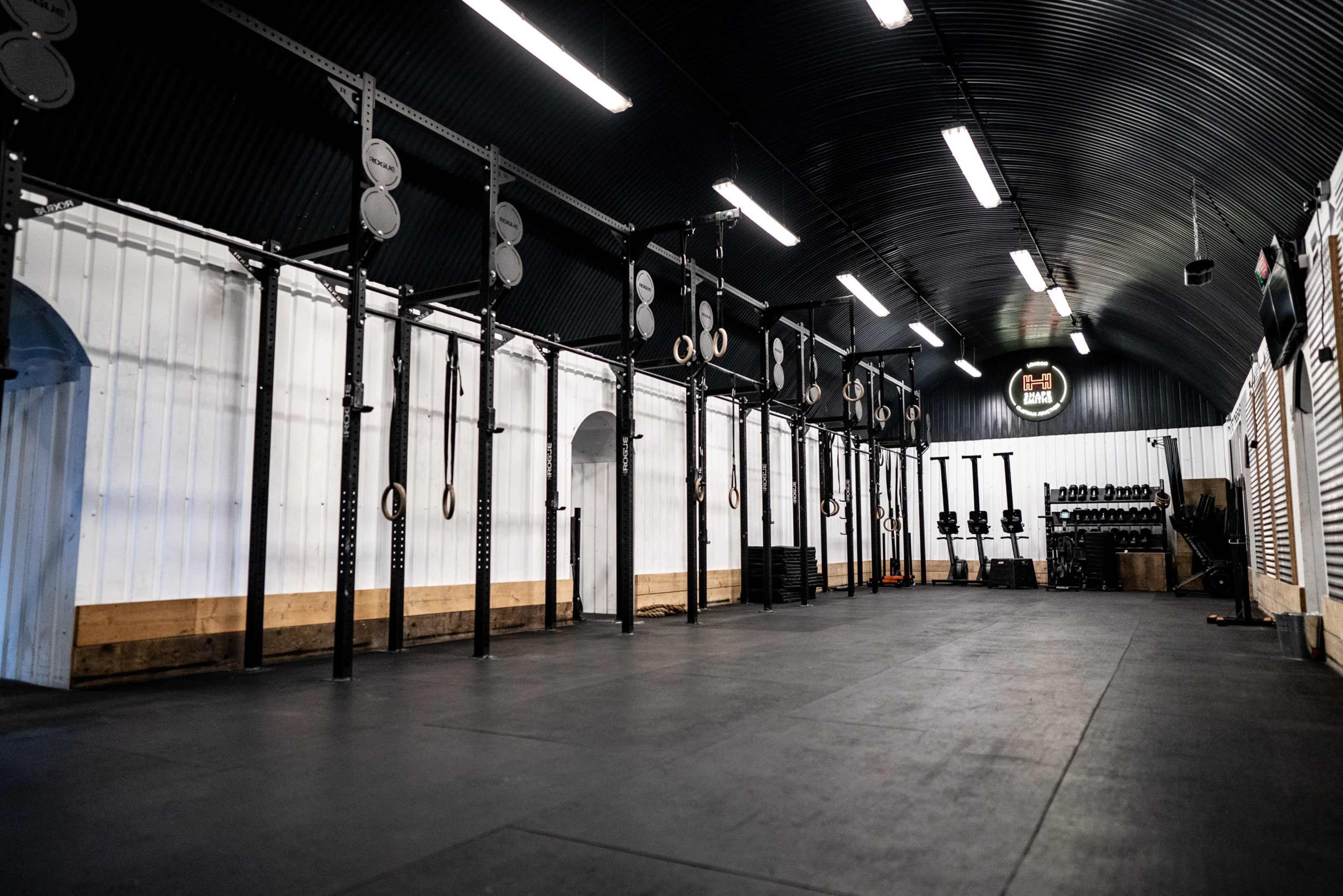 The image shows an indoor gym space equipped with exercise equipment, including pull-up bars, weightlifting racks, and fitness machines.