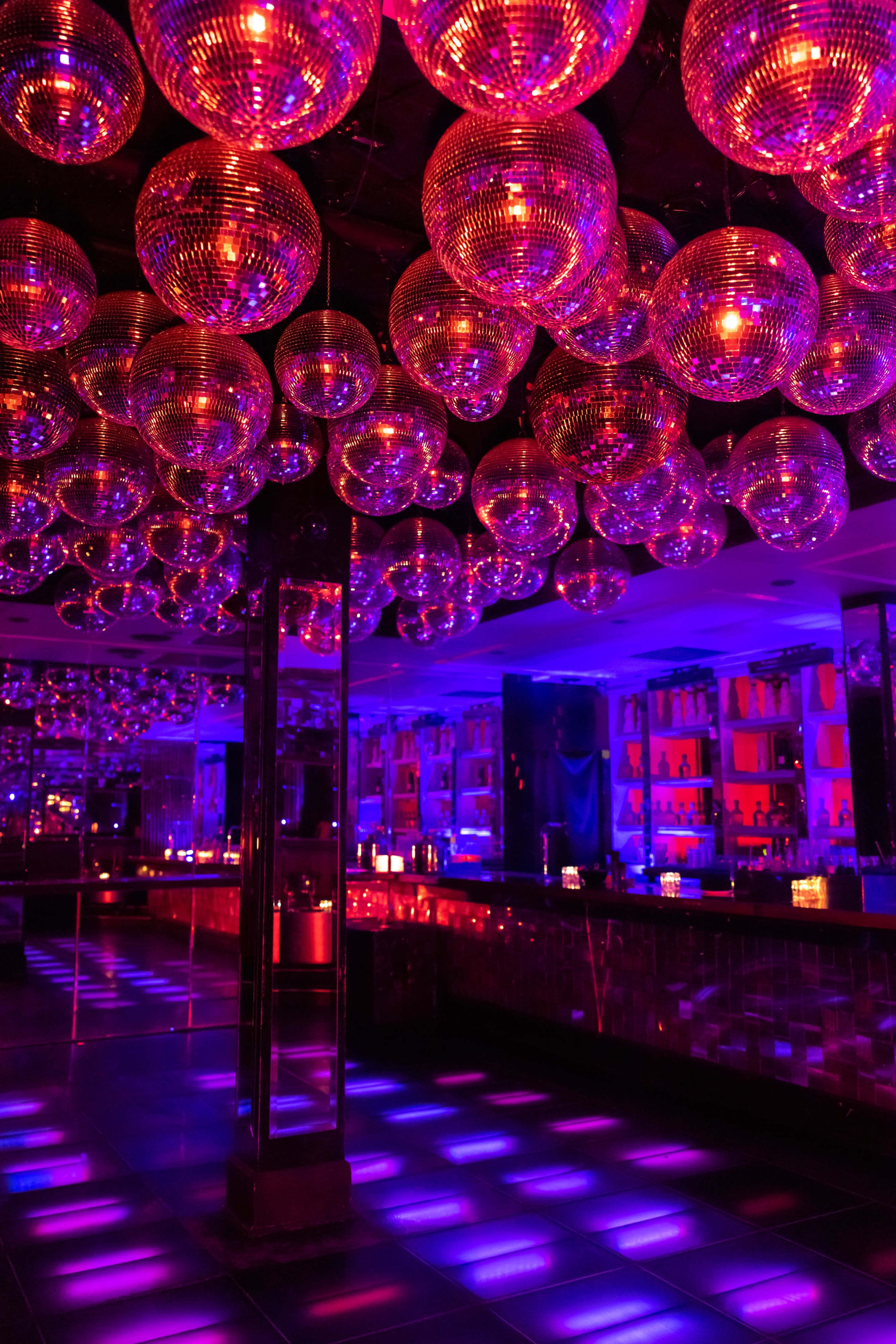 The scene shows a dimly lit nightclub with numerous disco balls hanging from the ceiling, creating vibrant reflections on the floor.