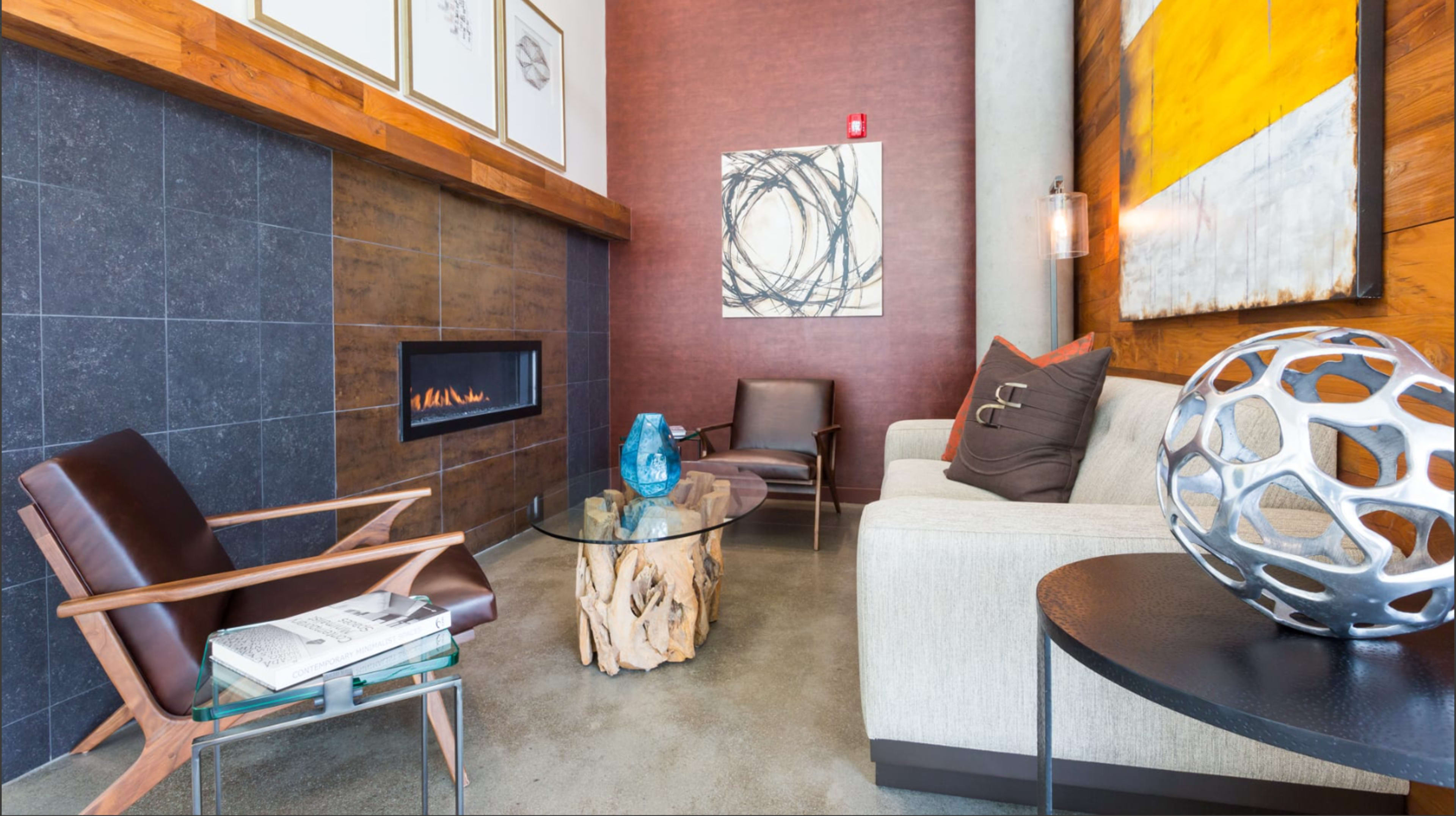 A modern lounge area featuring a sofa, an armchair, a glass coffee table on a wooden base, and a linear fireplace against a textured wall.