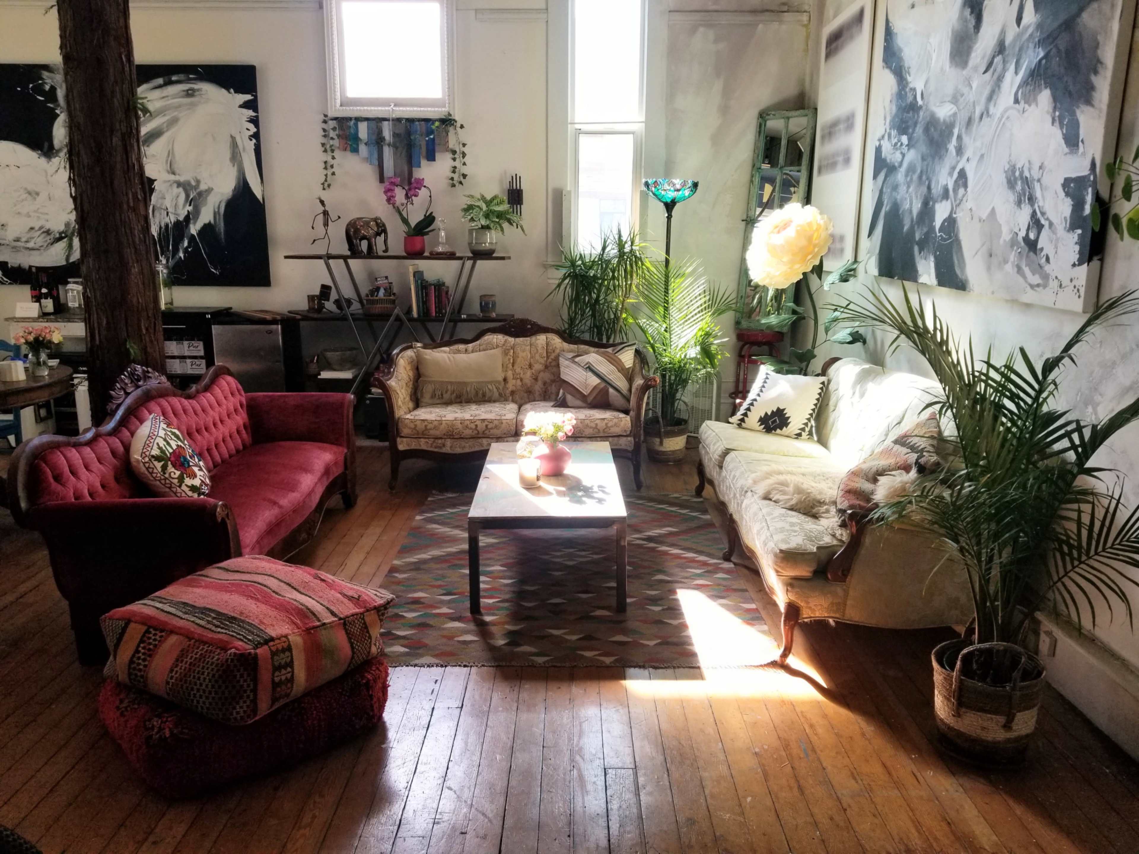 A cozy living room features eclectic furniture, including two sofas and a coffee table, surrounded by plants and artwork on the walls.