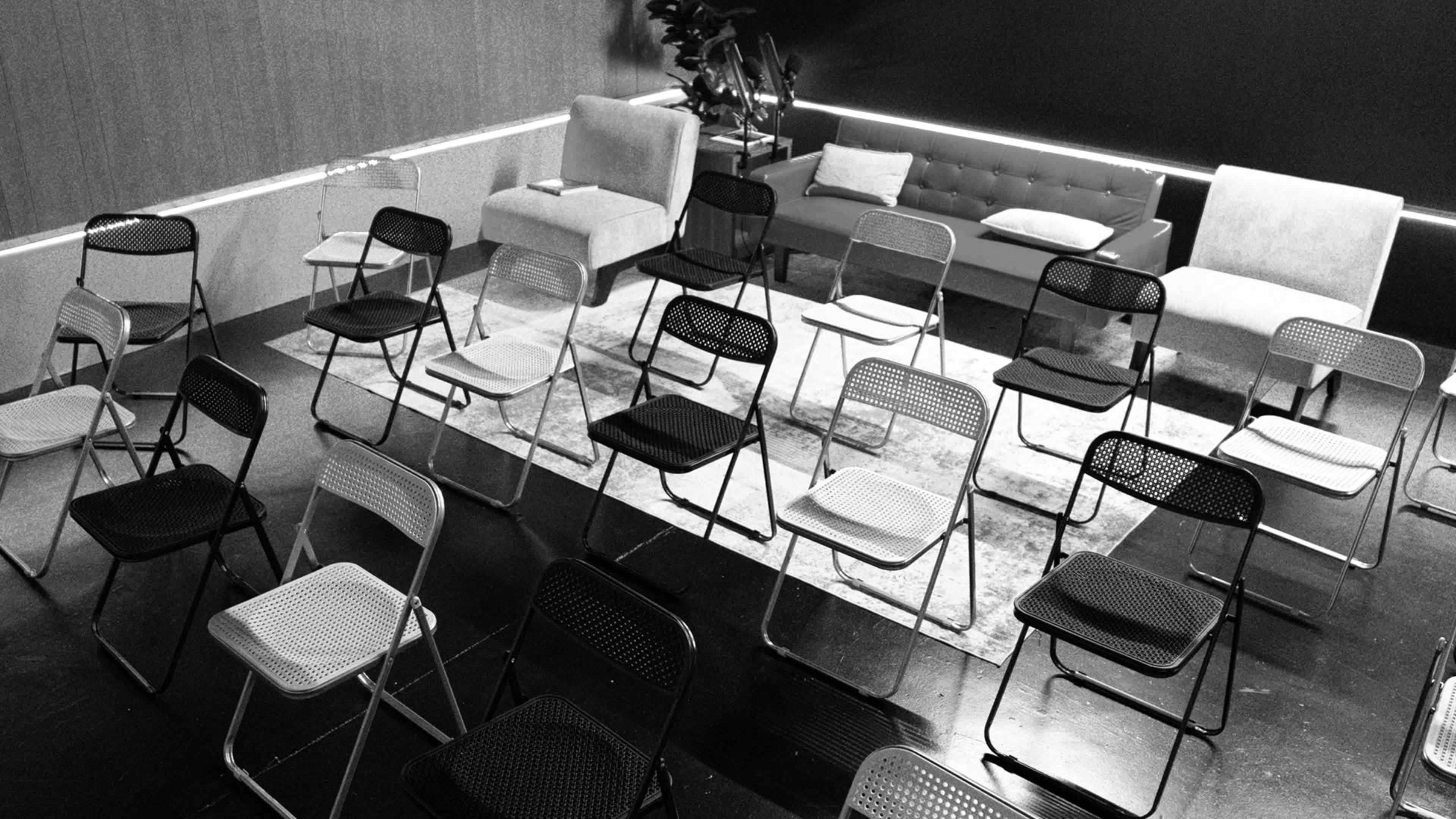 The image shows a room arranged with several folding chairs placed in a grid pattern, with a couple of couches on one side.