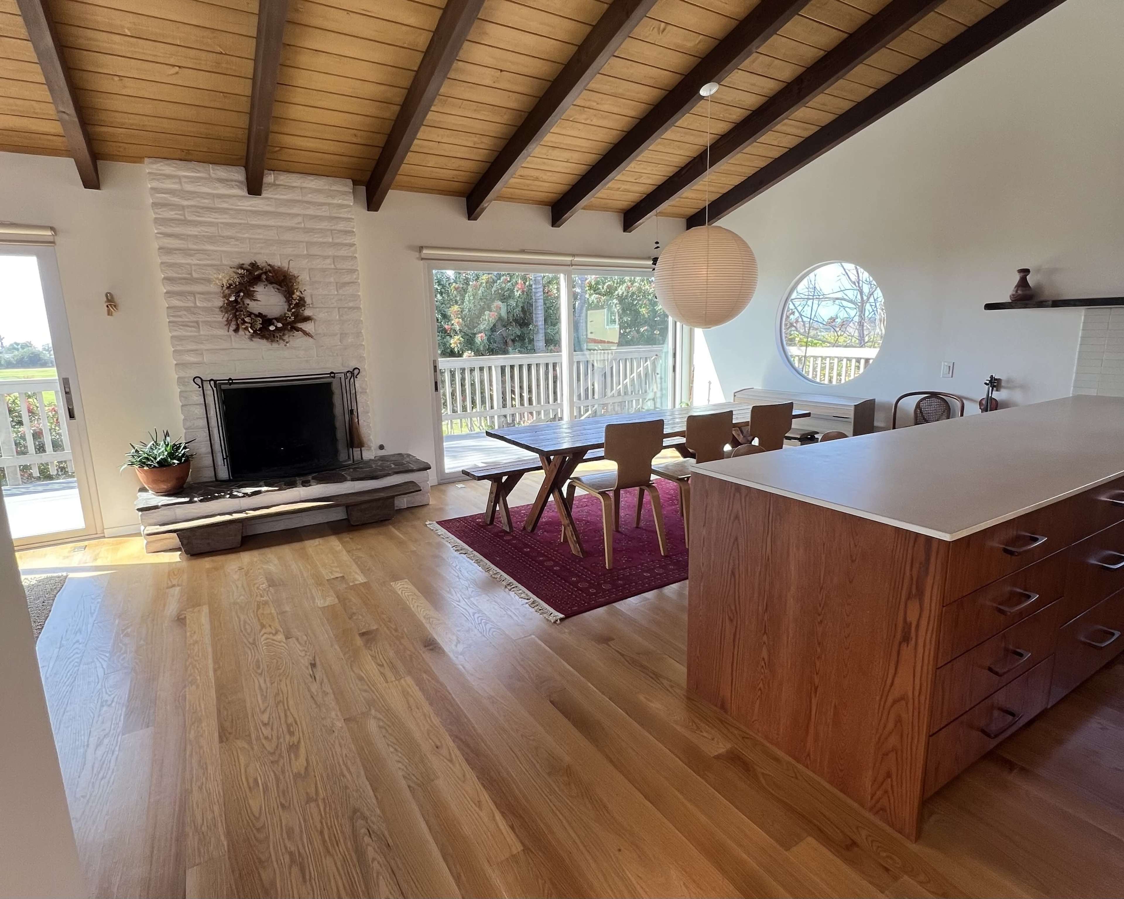 The image showcases an open-concept living space featuring a dining area with a wooden table, a fireplace with a stone facade, and large windows that allow natural light to fill the room.