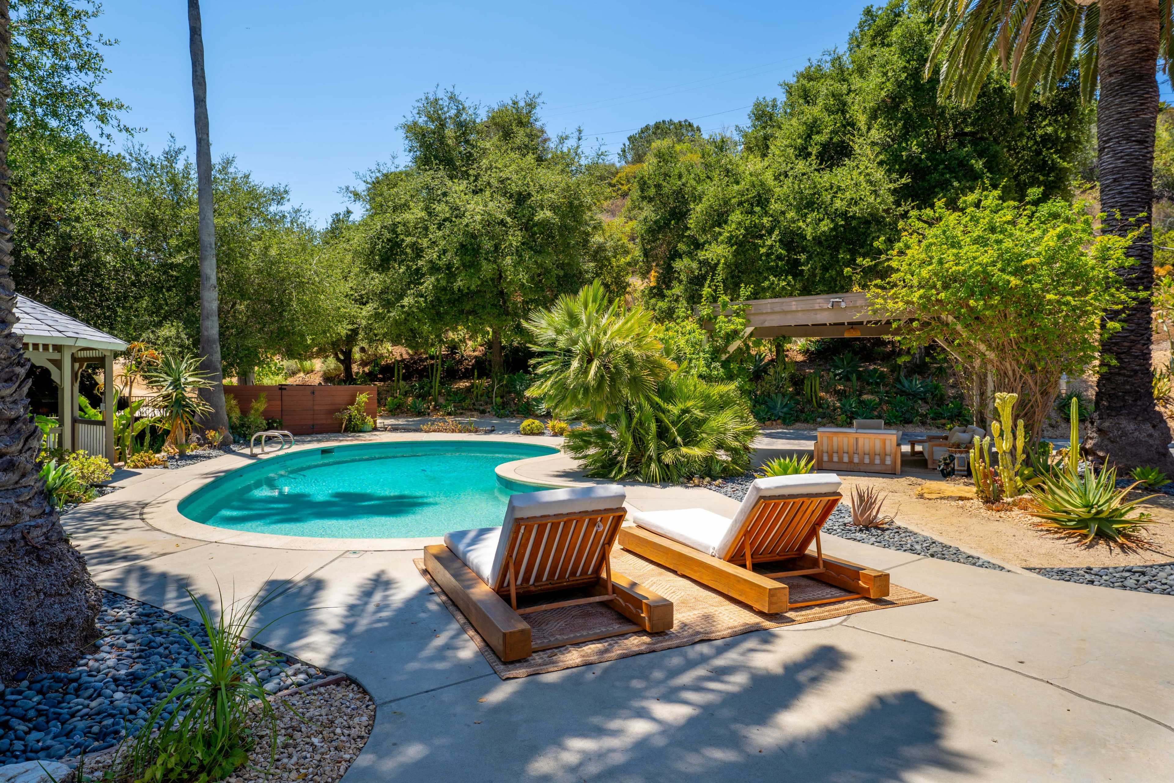 A swimming pool surrounded by tropical plants and two lounge chairs on a patio.