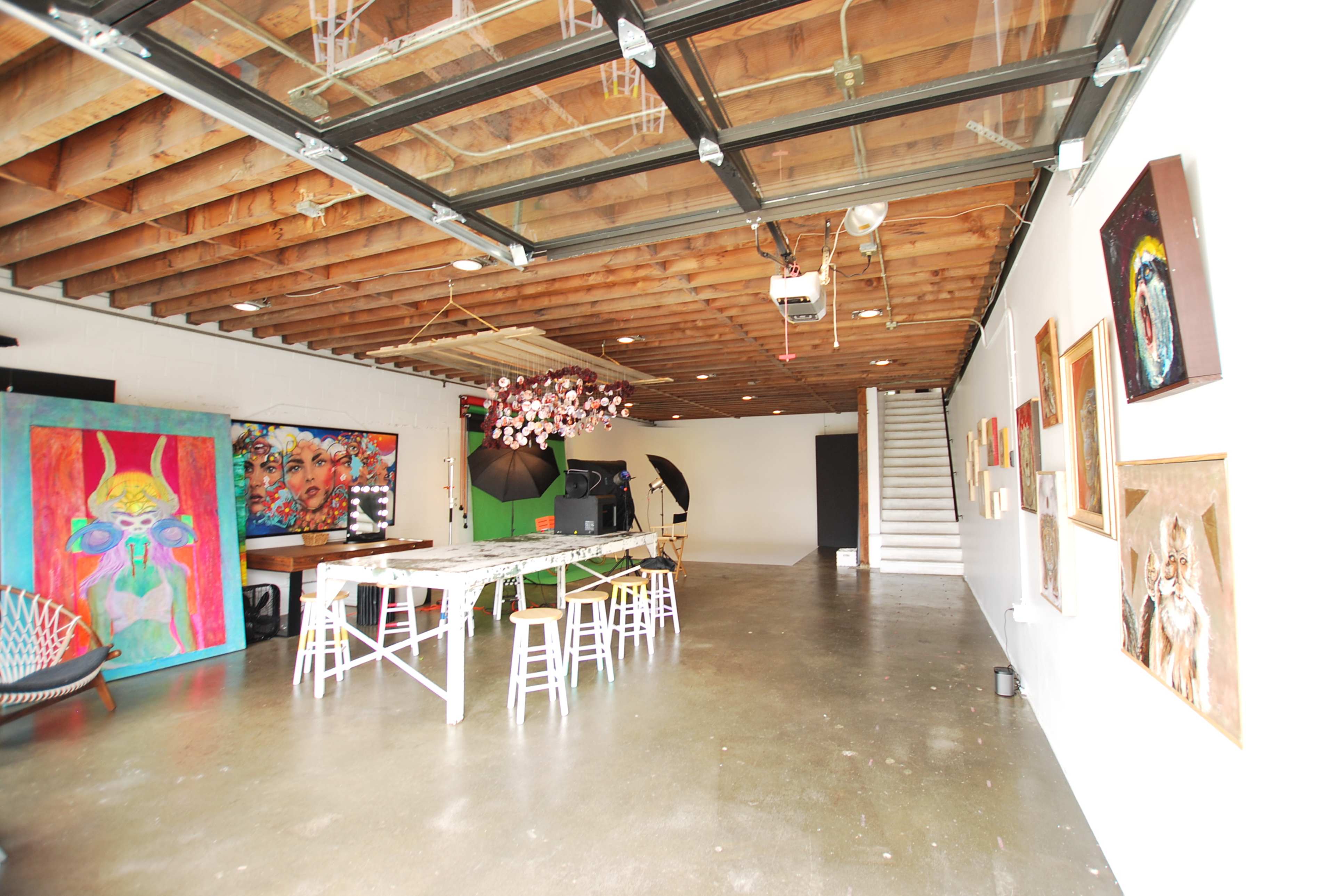 The image shows an open art studio with a long table, wooden beams overhead, and various artworks displayed on the walls.