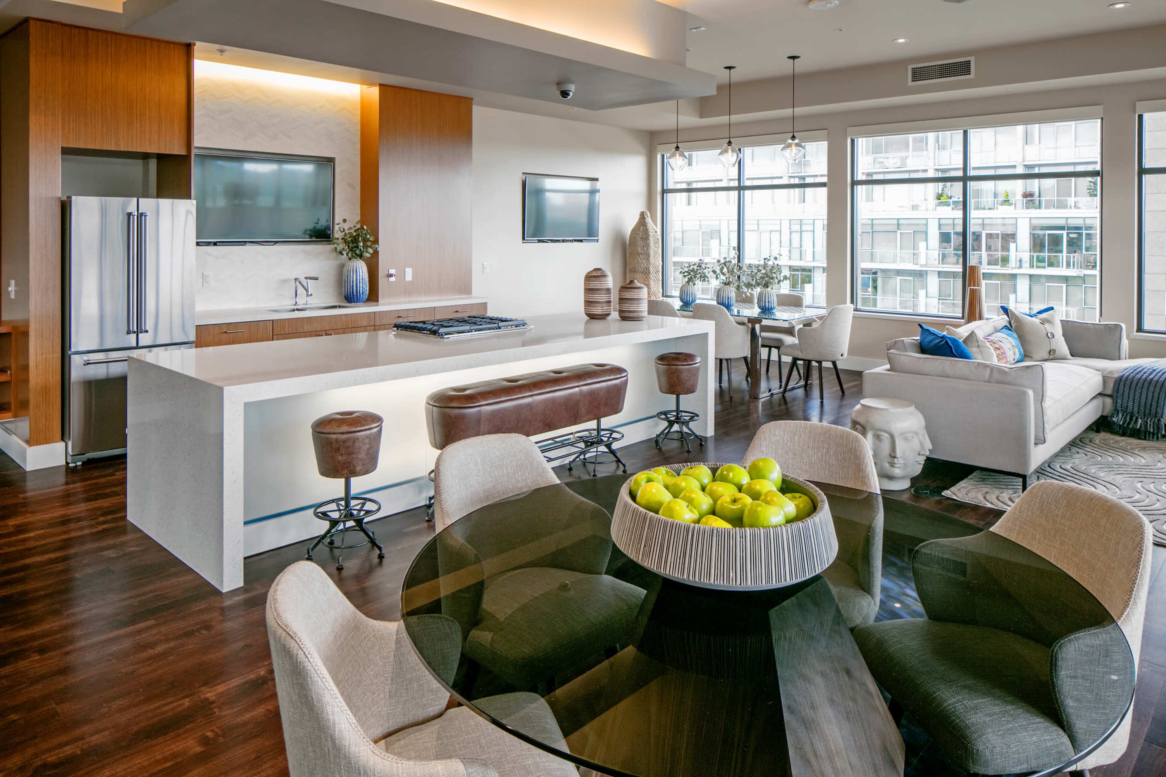 A modern living space featuring a kitchen island, dining table, and a seating area with large windows allowing natural light.