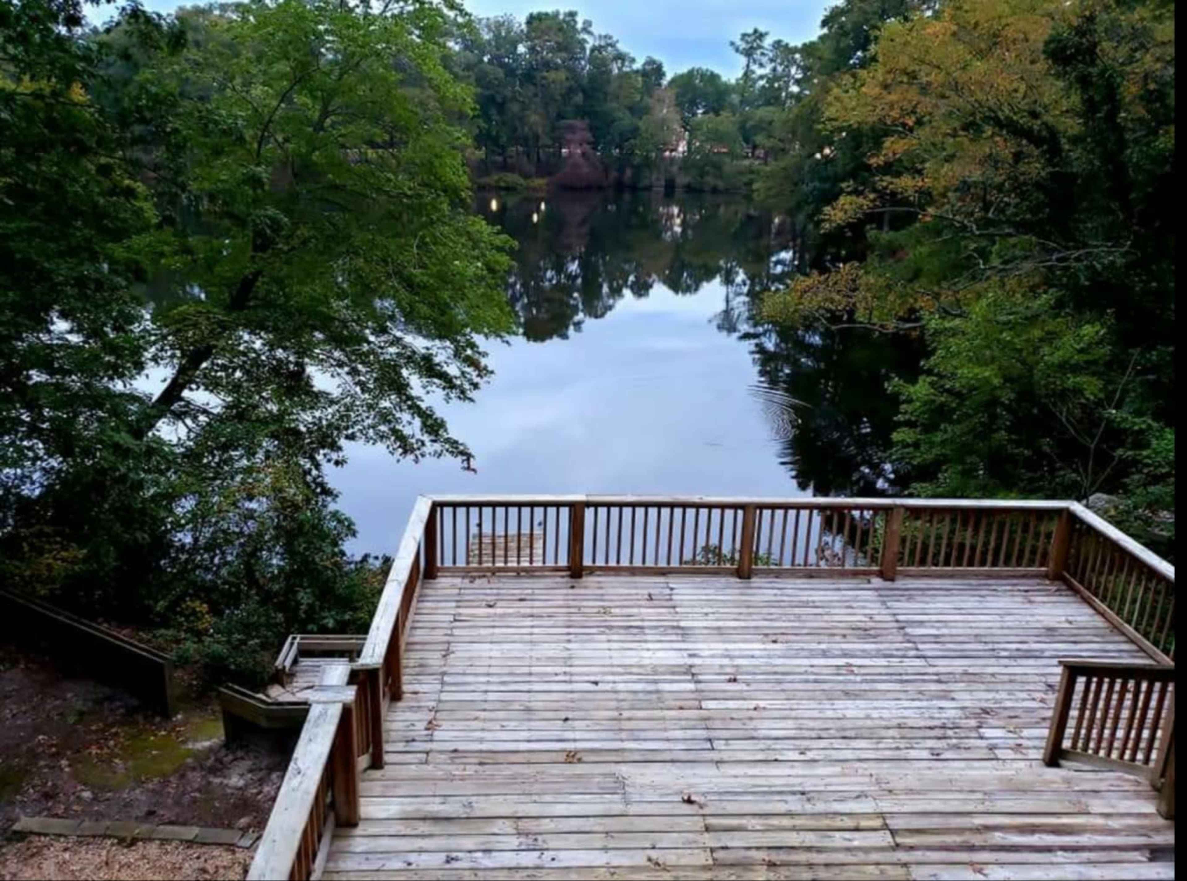 A wooden deck overlooks a calm body of water surrounded by trees.