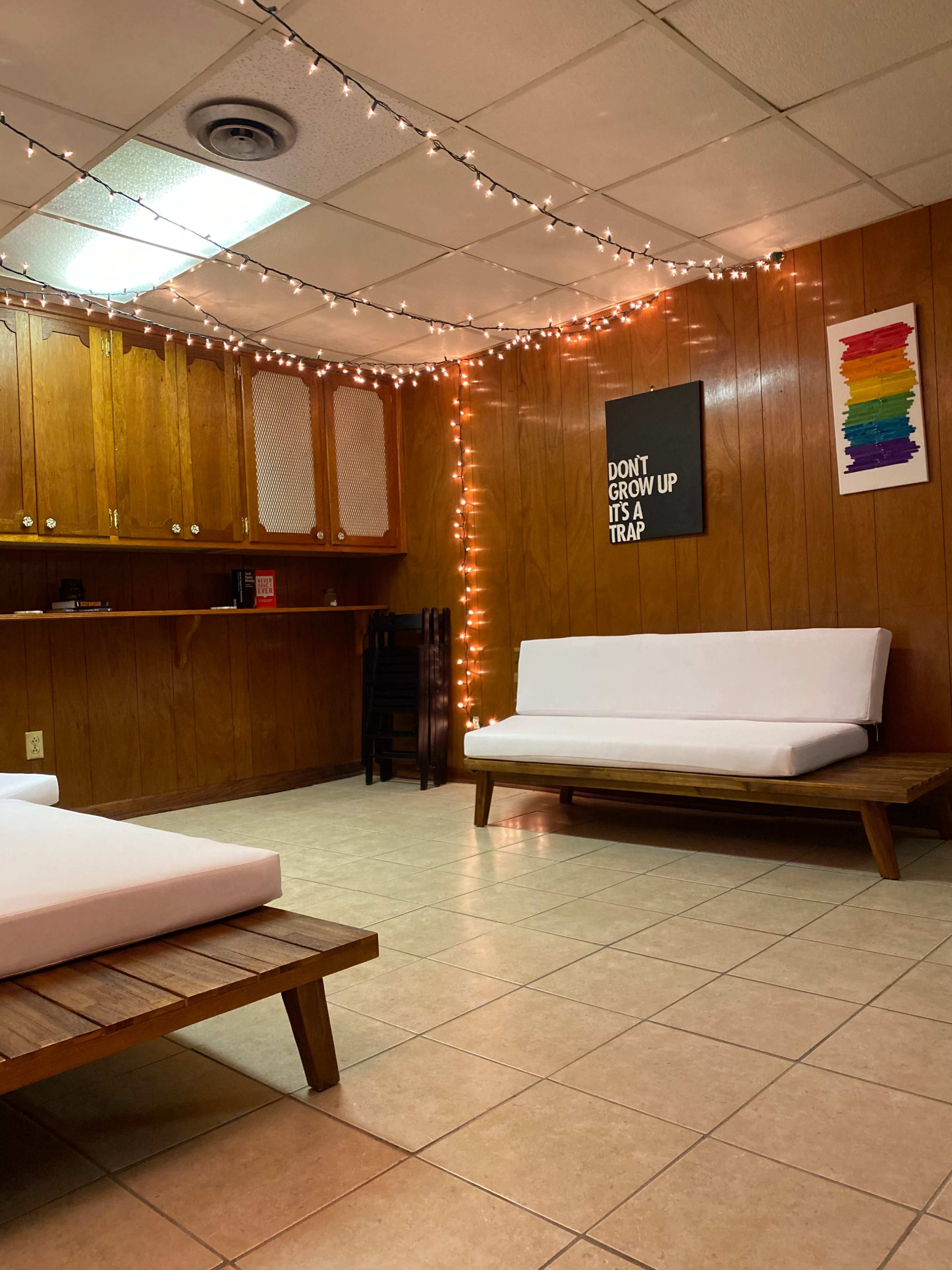 A room with wooden paneling, tiled flooring, soft seating, and string lights hanging on the walls alongside a framed poster.