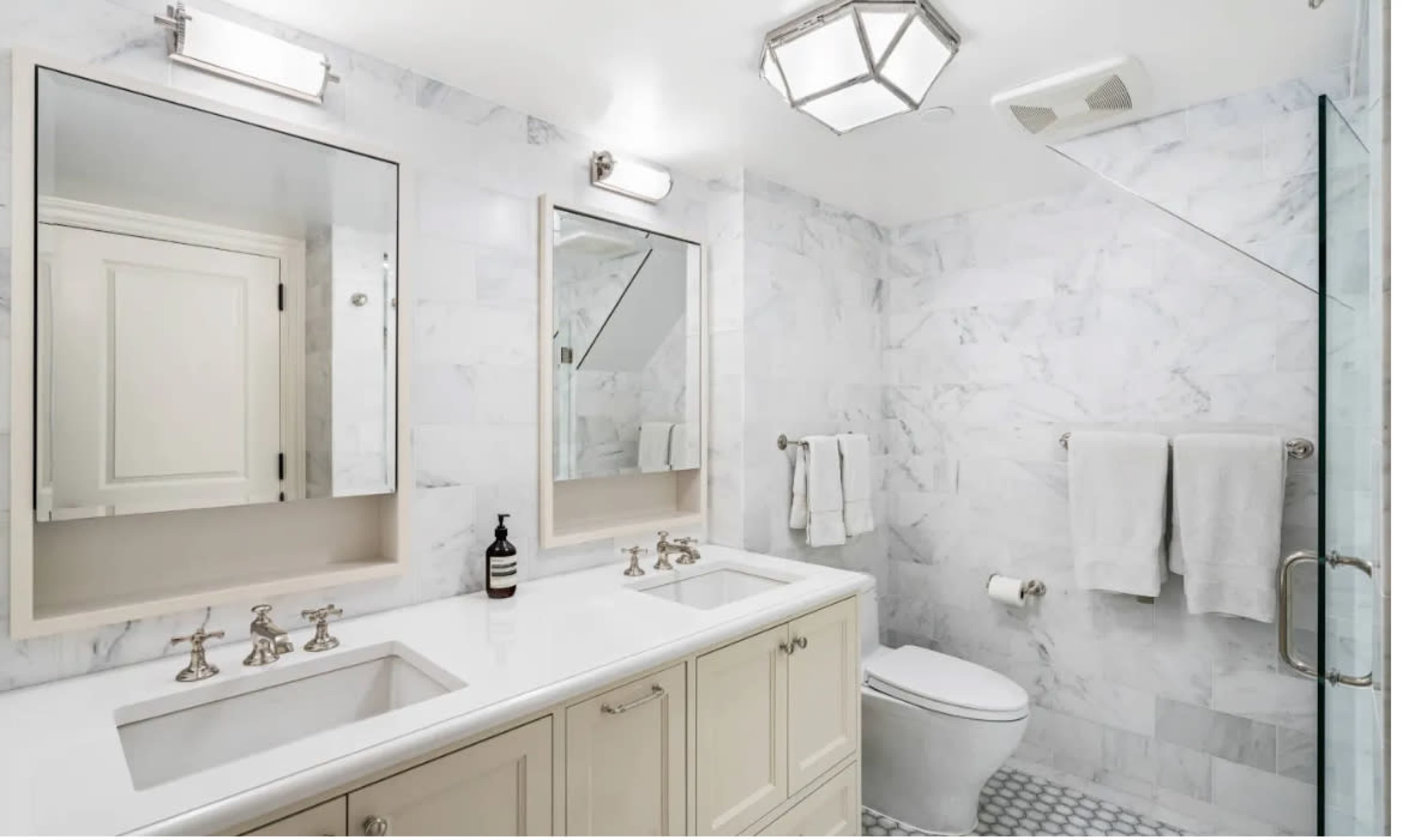 The image shows a modern bathroom featuring a double vanity with two sinks, framed mirrors, and light fixtures, along with a white marble wall and floor design.