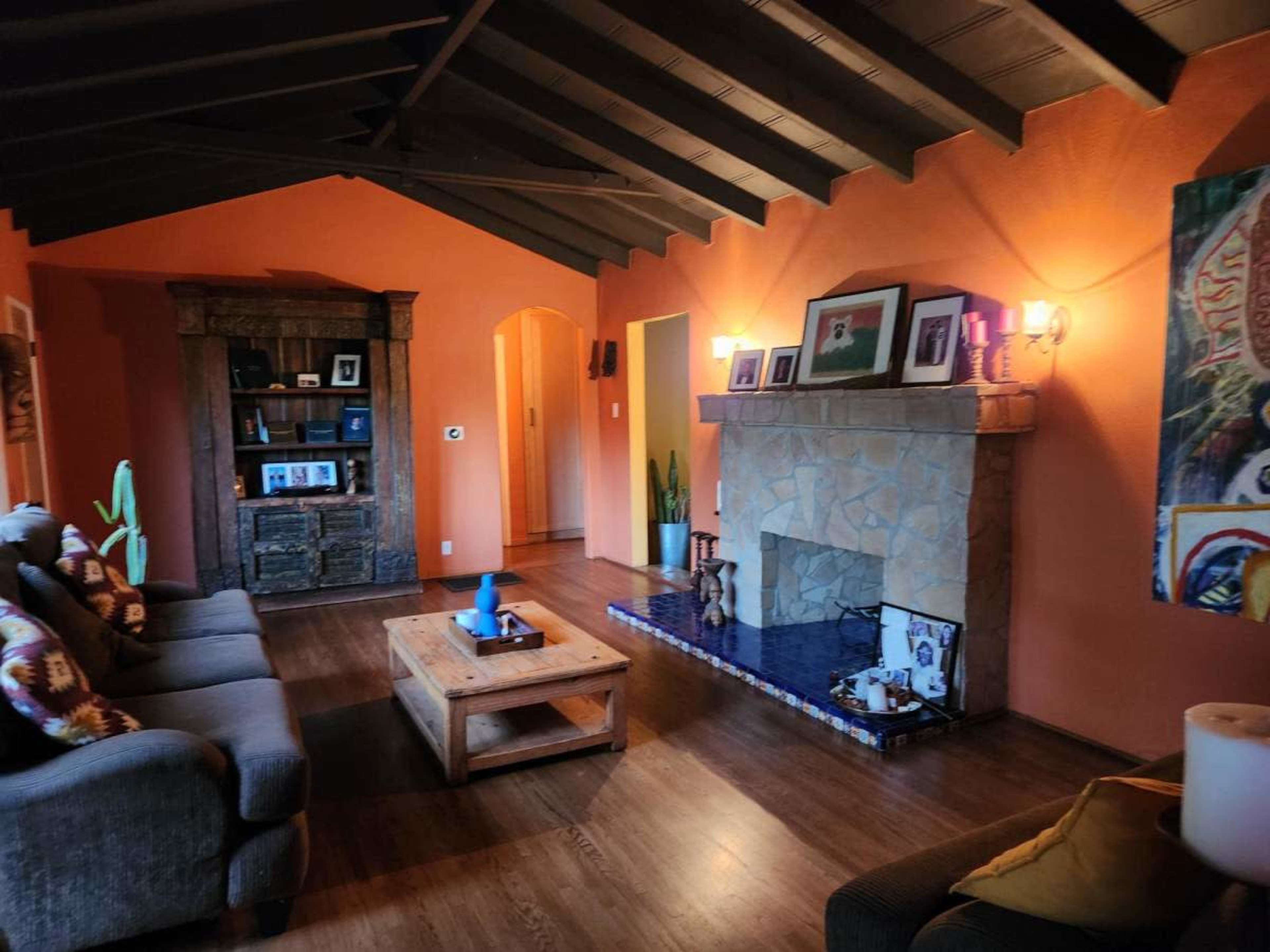 The image shows a living room with orange walls, a stone fireplace, a wooden coffee table, and a dark wooden bookshelf.