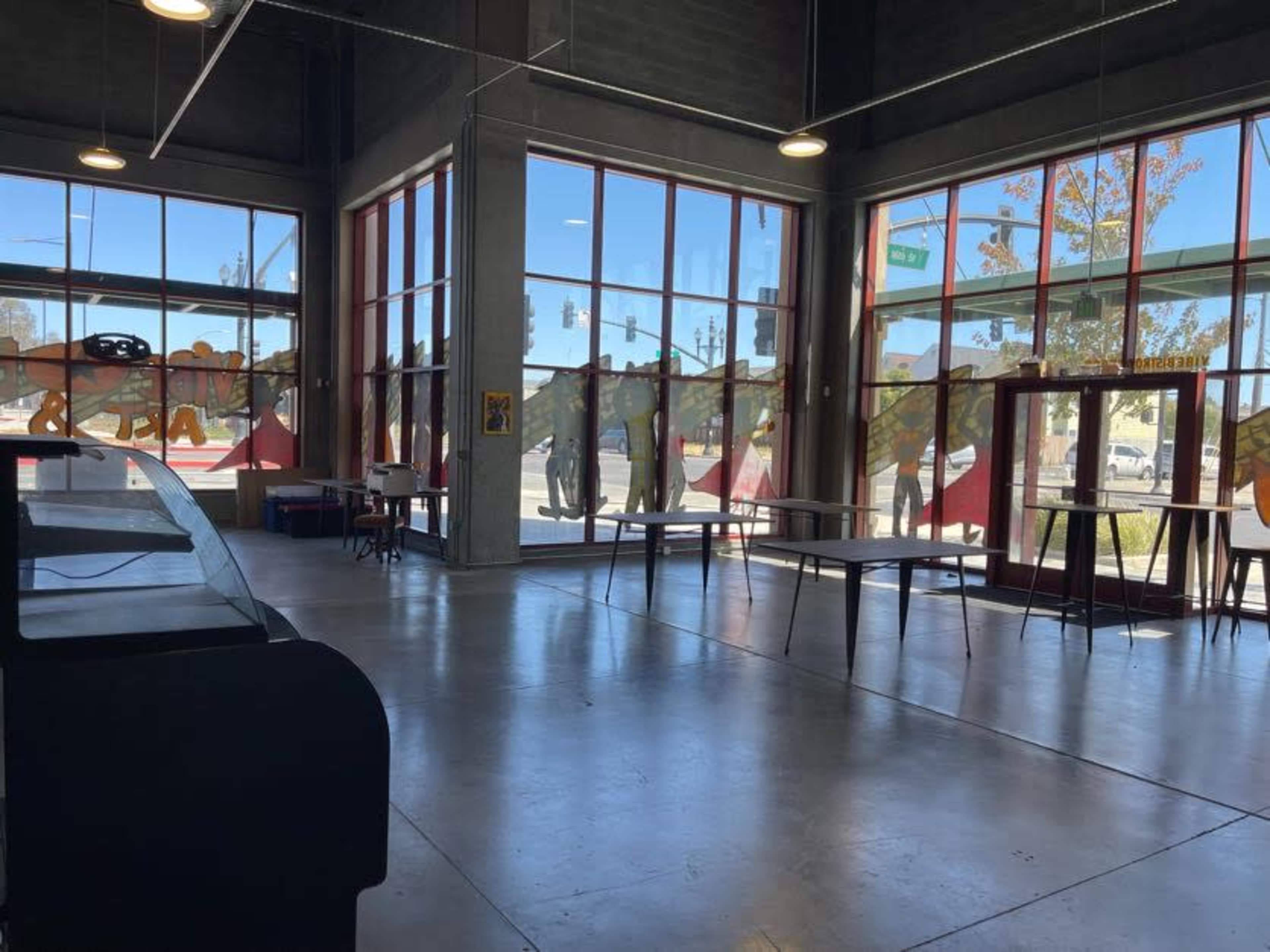 A spacious indoor area with large windows, empty tables, and a view of an outdoor scene.
