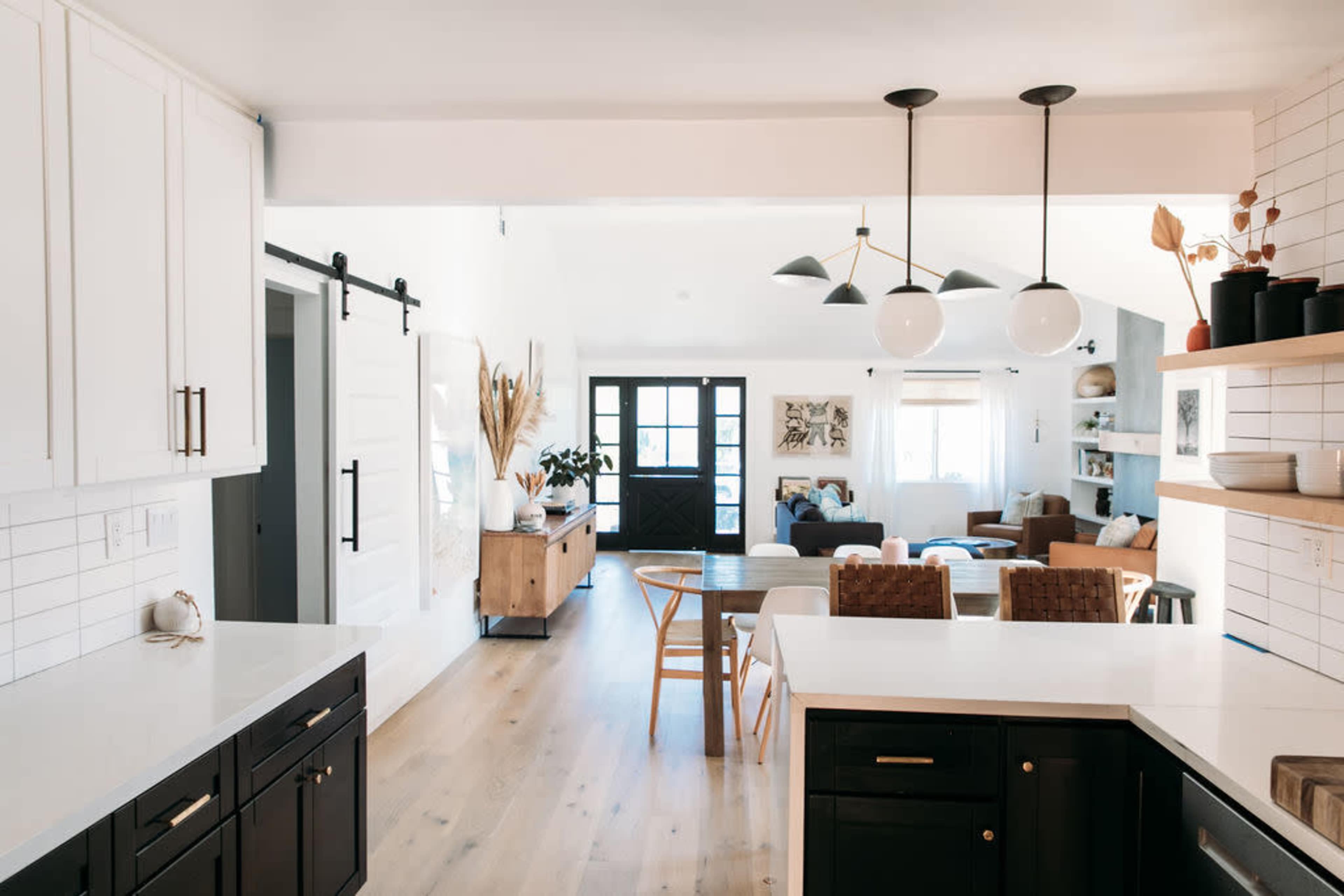 A modern kitchen with white cabinetry and a spacious open living area featuring a seating arrangement and natural light.