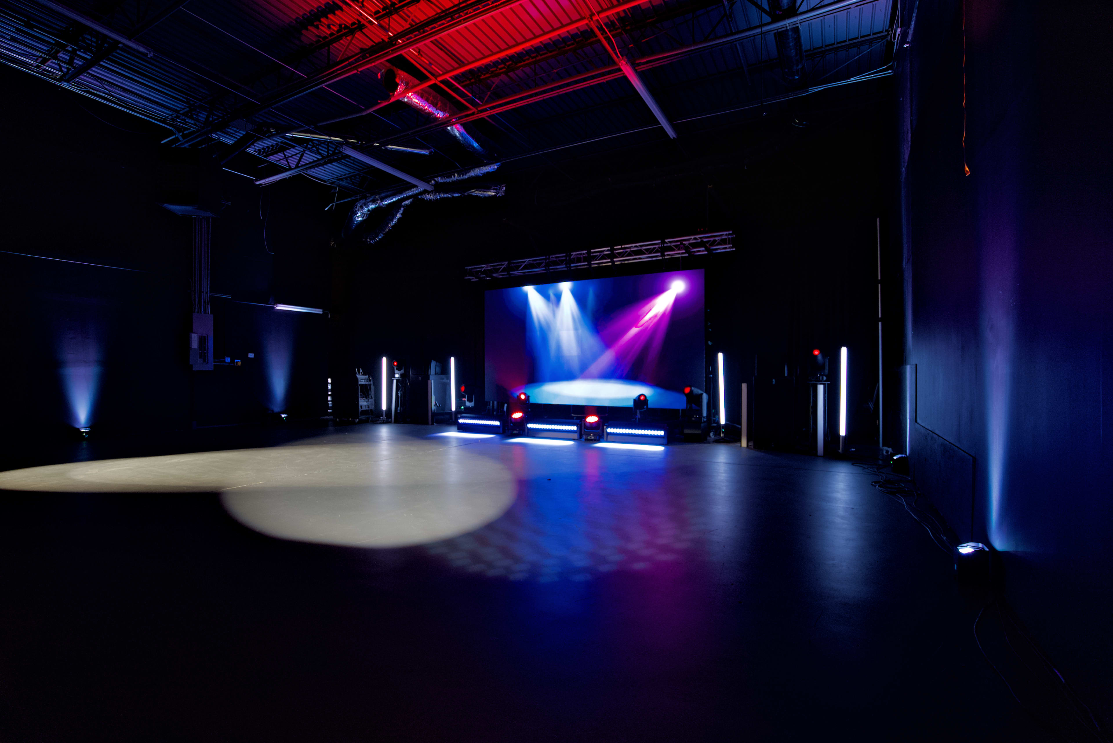 A dimly lit performance space features a raised stage illuminated by colorful lights.