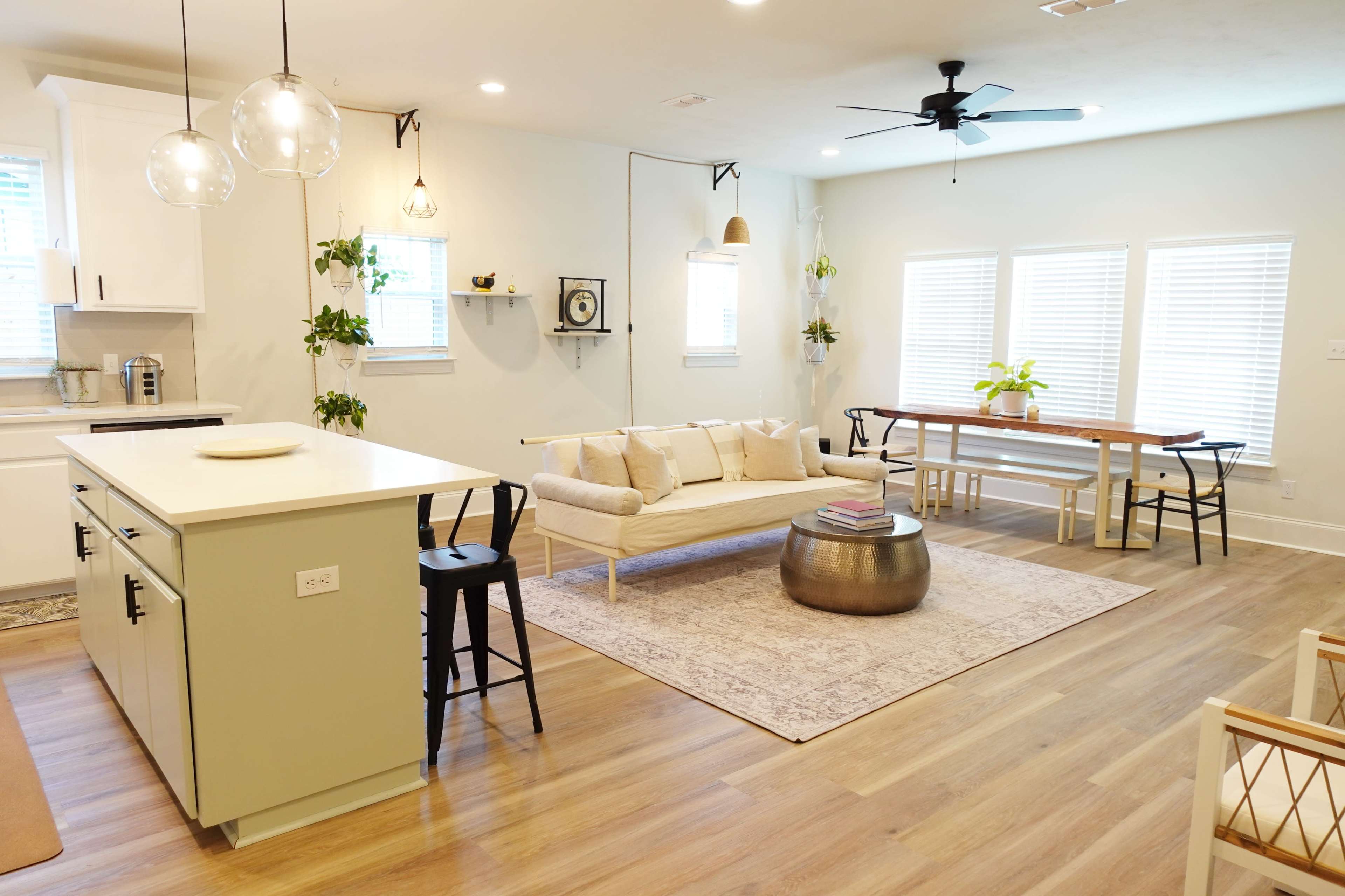 A modern living space featuring a light-colored sofa, a round coffee table, a dining area with a wooden table, and large windows letting in natural light.