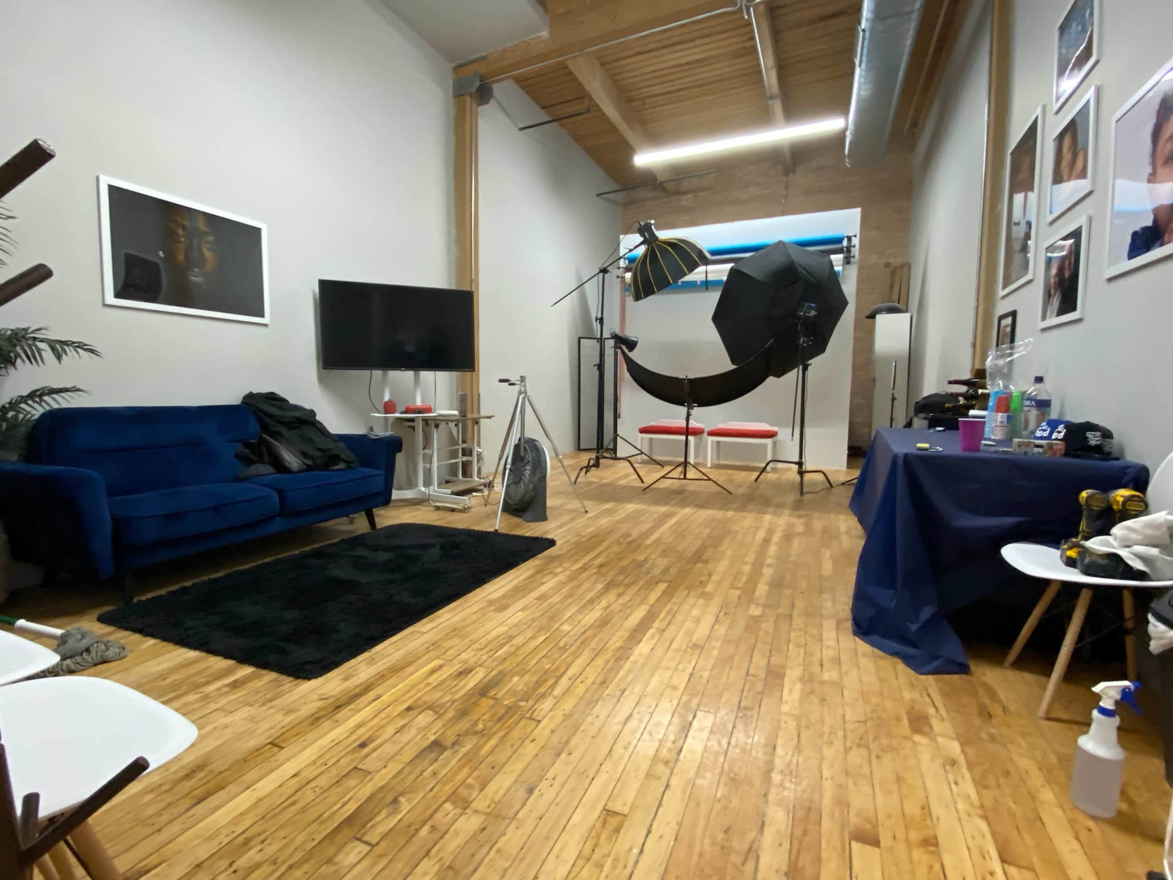A photography studio with hardwood floors, a blue couch, a television, and a setup for a photoshoot featuring a large umbrella light and backdrop.