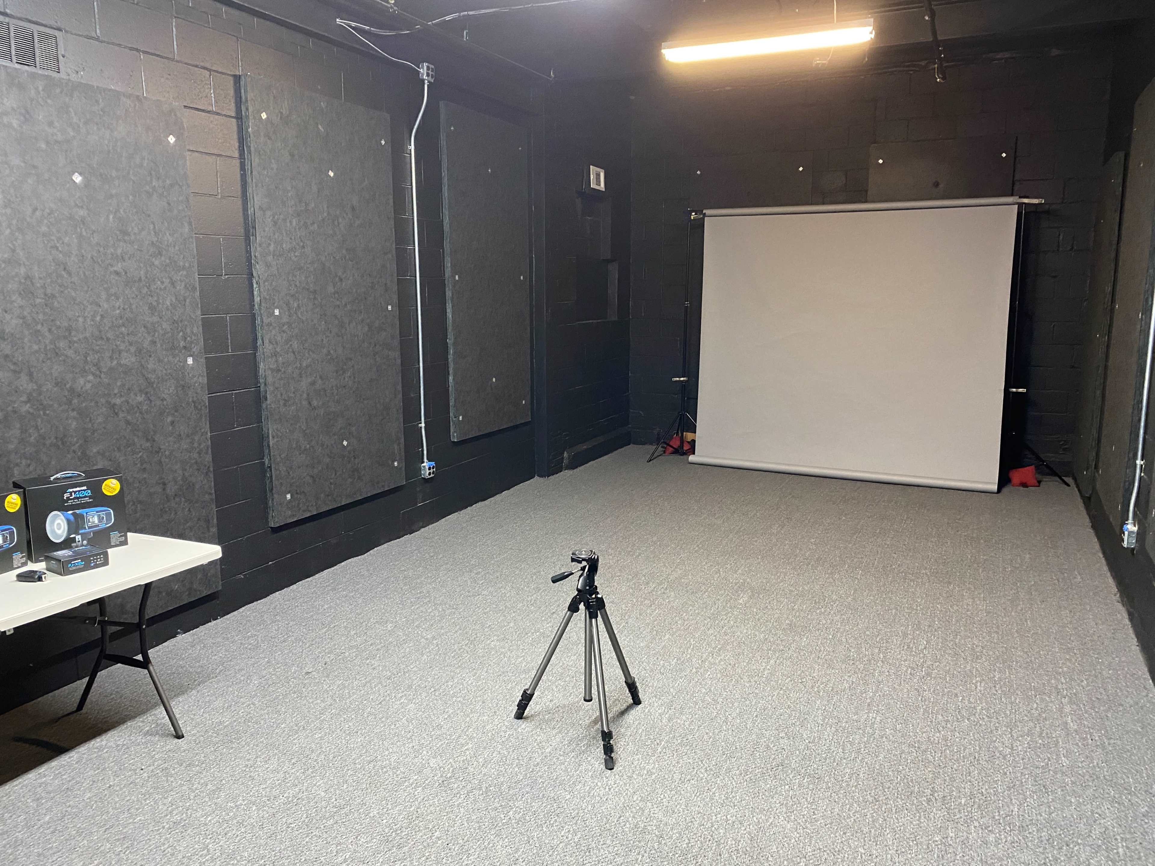 A spacious black-walled room features a blank projection screen and a tripod on a table.