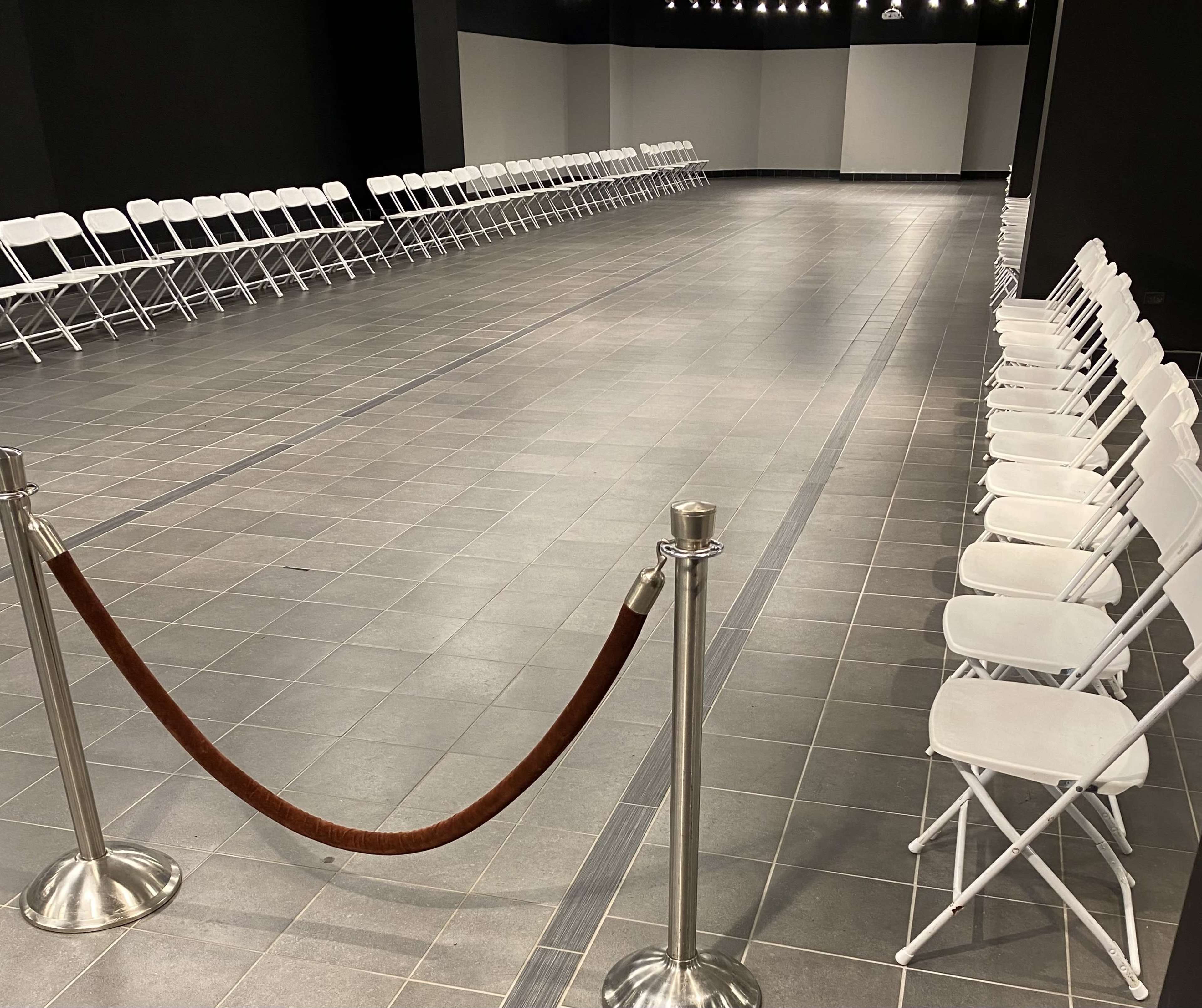 A spacious room with white folding chairs arranged in two parallel lines along a tiled floor.