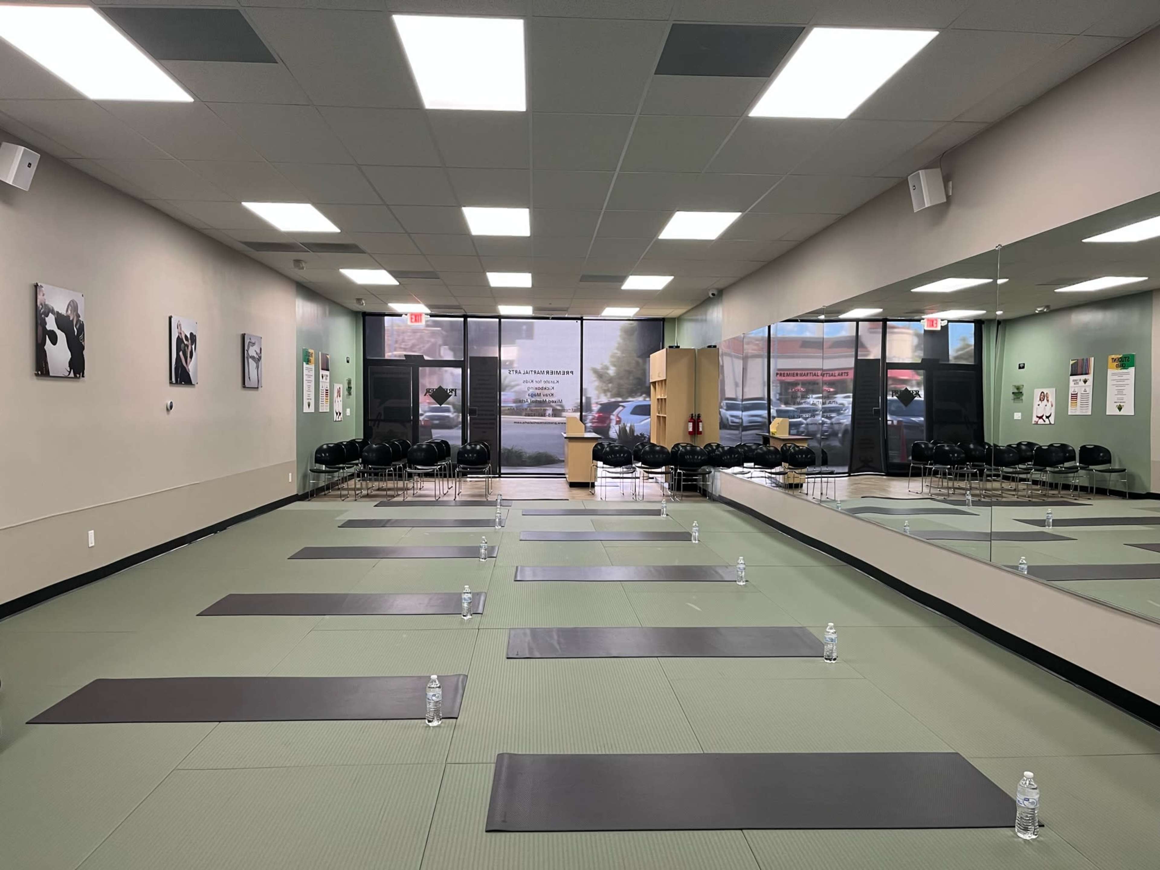 A yoga studio with several mats arranged on a green floor, water bottles placed on each mat, and a large mirror reflecting the room's interior.