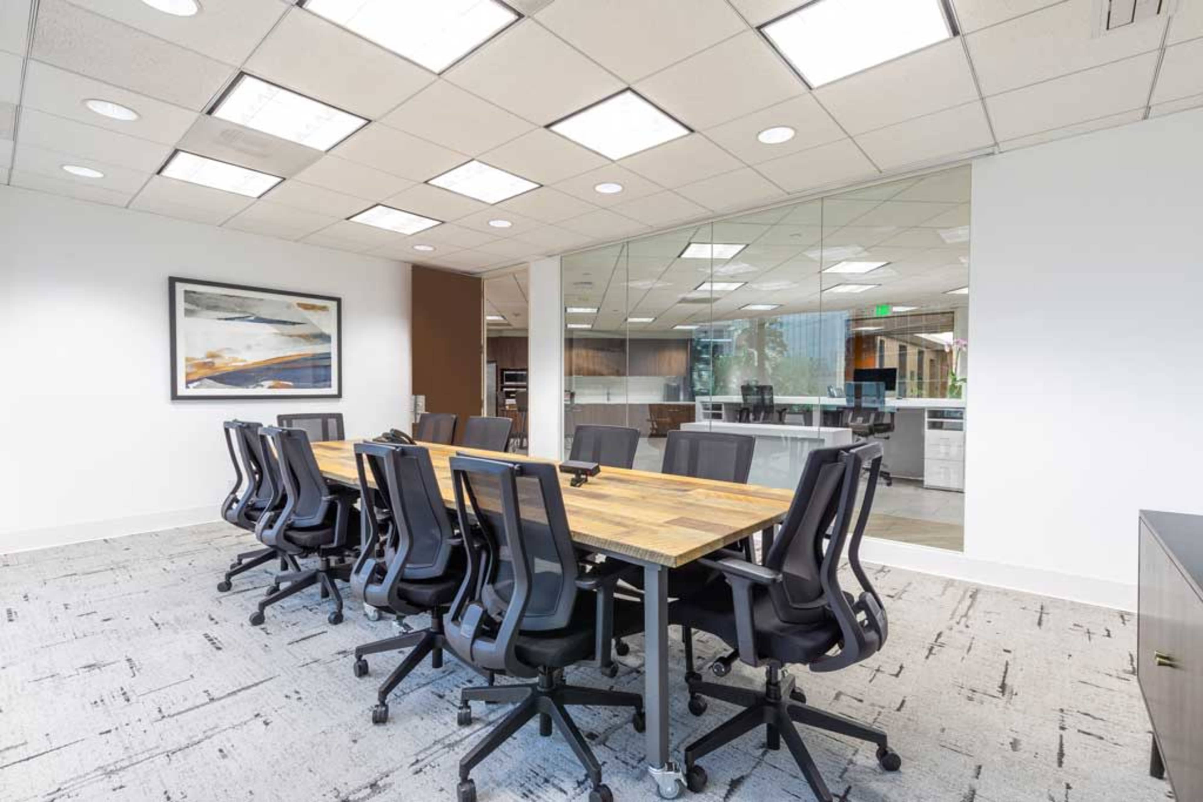 A large conference table with several ergonomic chairs is set up in a modern office space with glass walls.