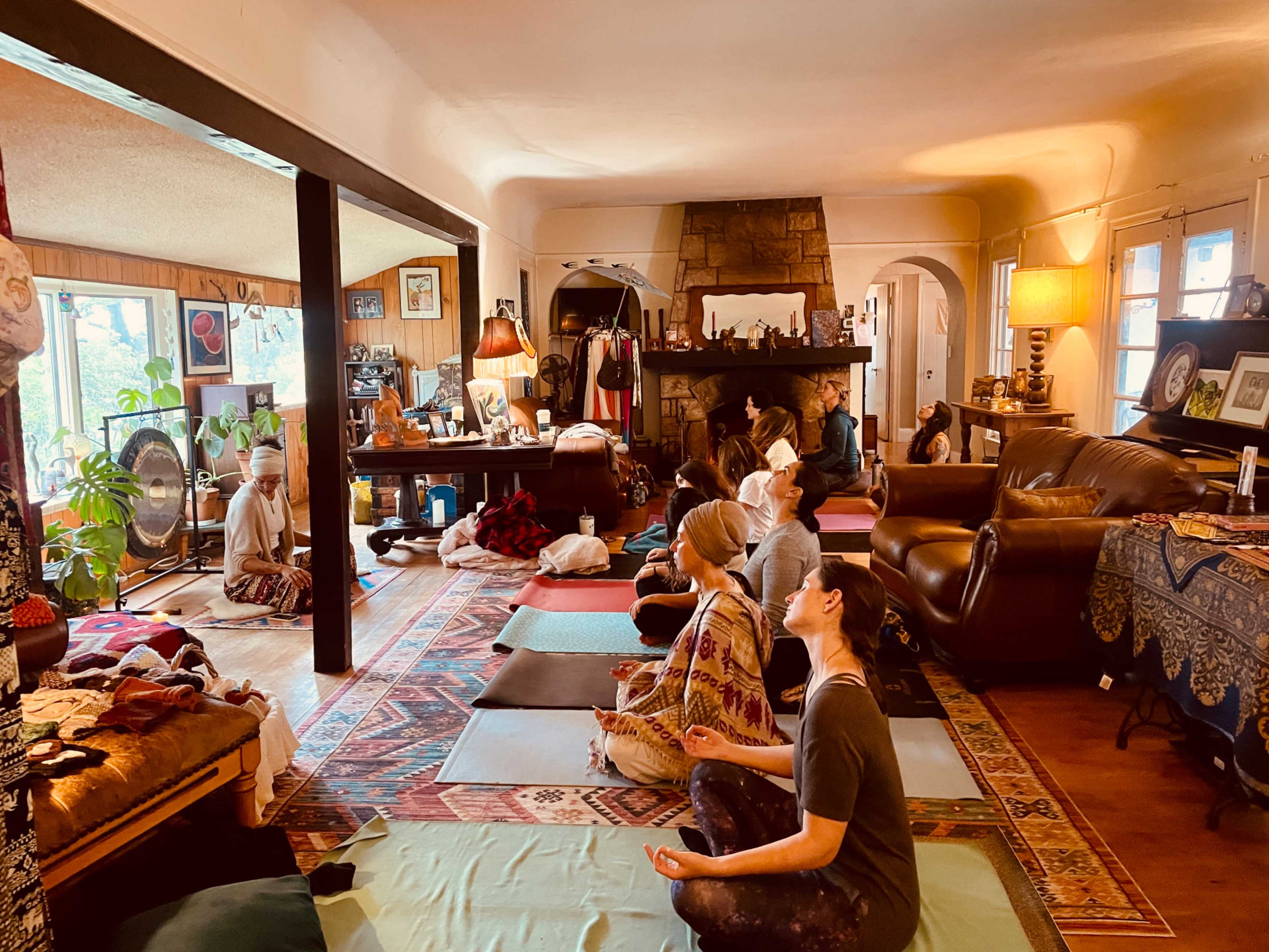 A group of people is practicing meditation in a cozy room filled with comfortable furnishings and natural light.