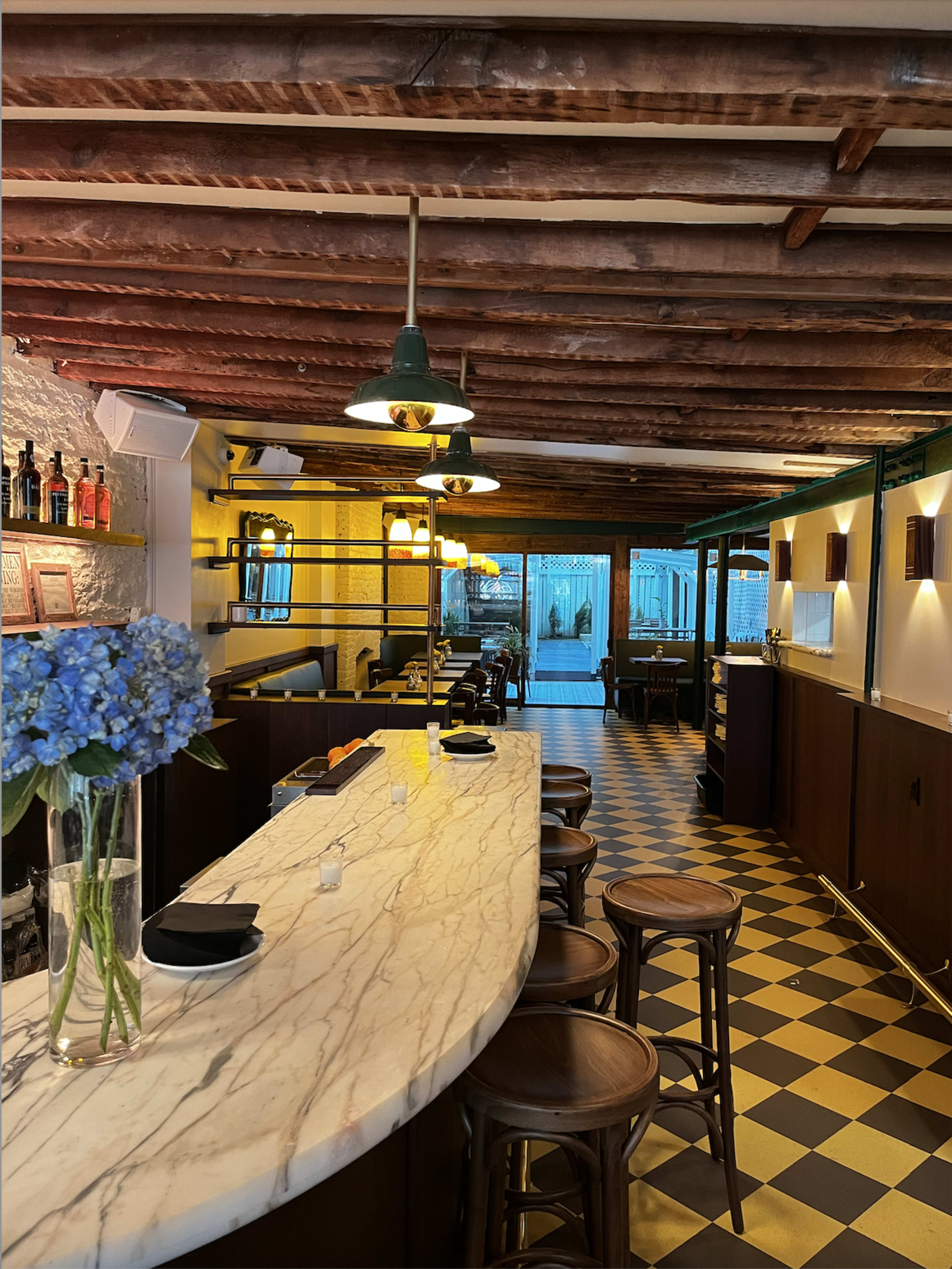 The image shows the interior of a restaurant with a marble bar, wooden stools, and a checkered floor.
