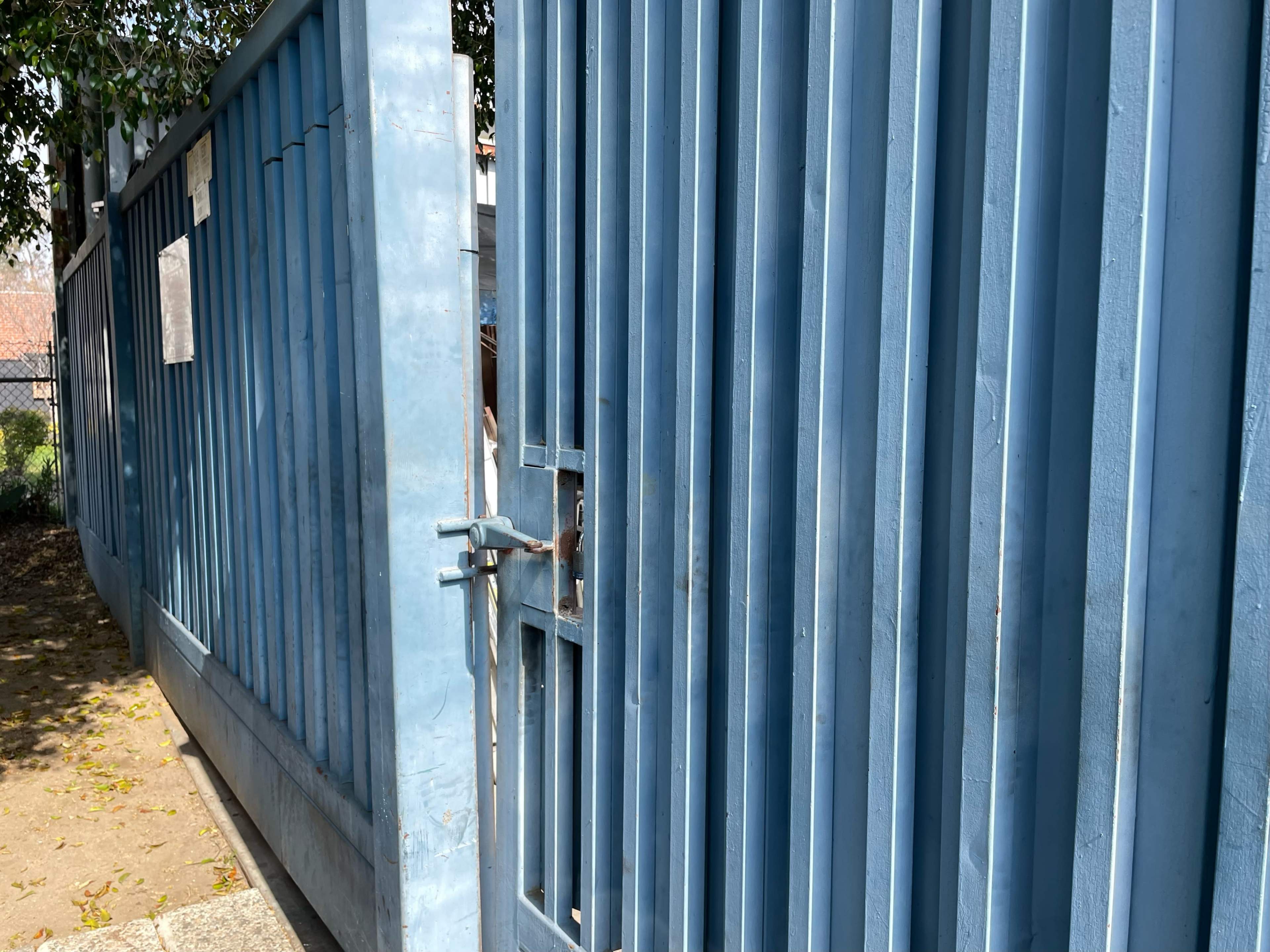 A blue metal gate stands ajar, revealing a pathway beyond it.