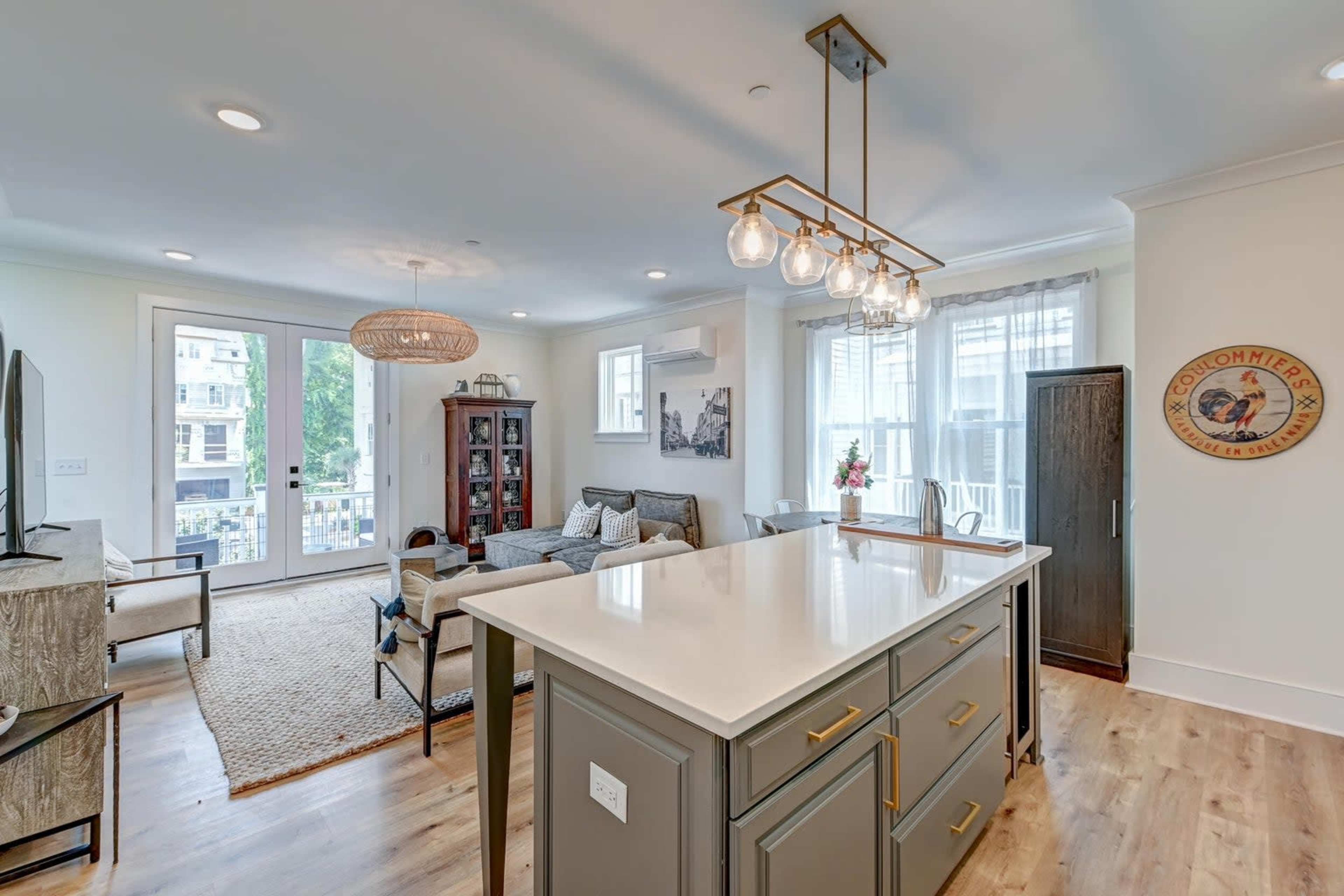A modern, open-concept living space featuring a kitchen island with pendant lighting, a cozy seating area, and large windows that allow natural light in.