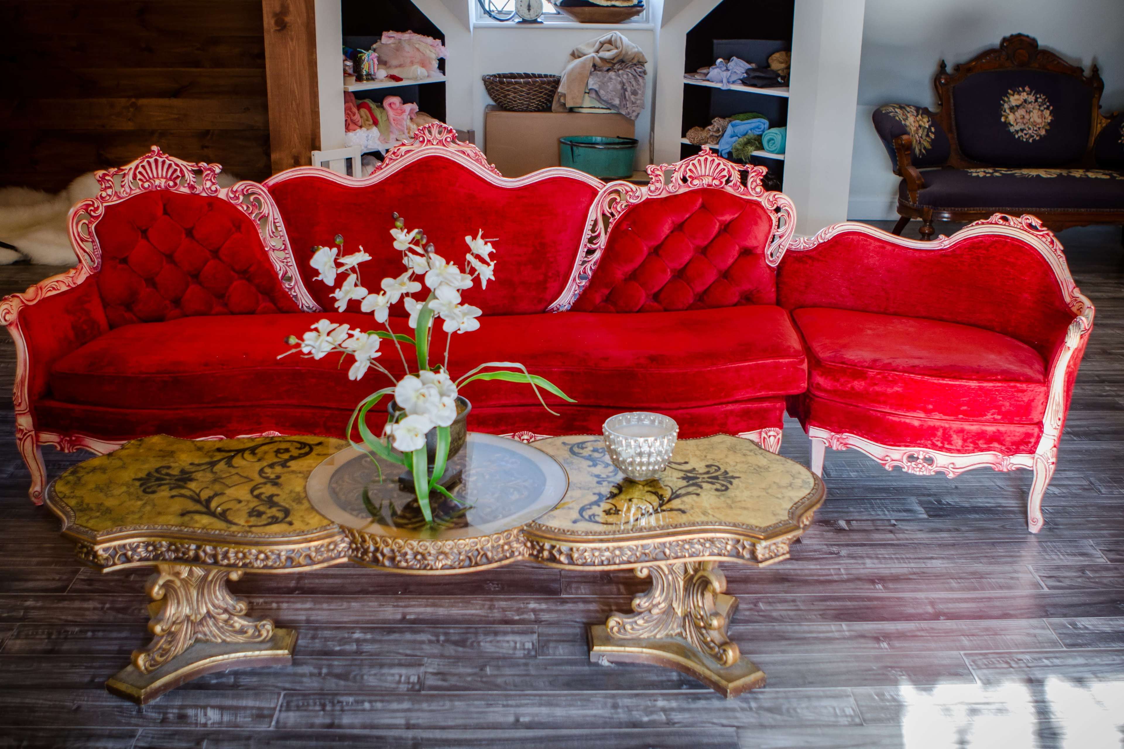 A red velvet sectional sofa with ornate pink accents and a golden, intricately designed coffee table in front.