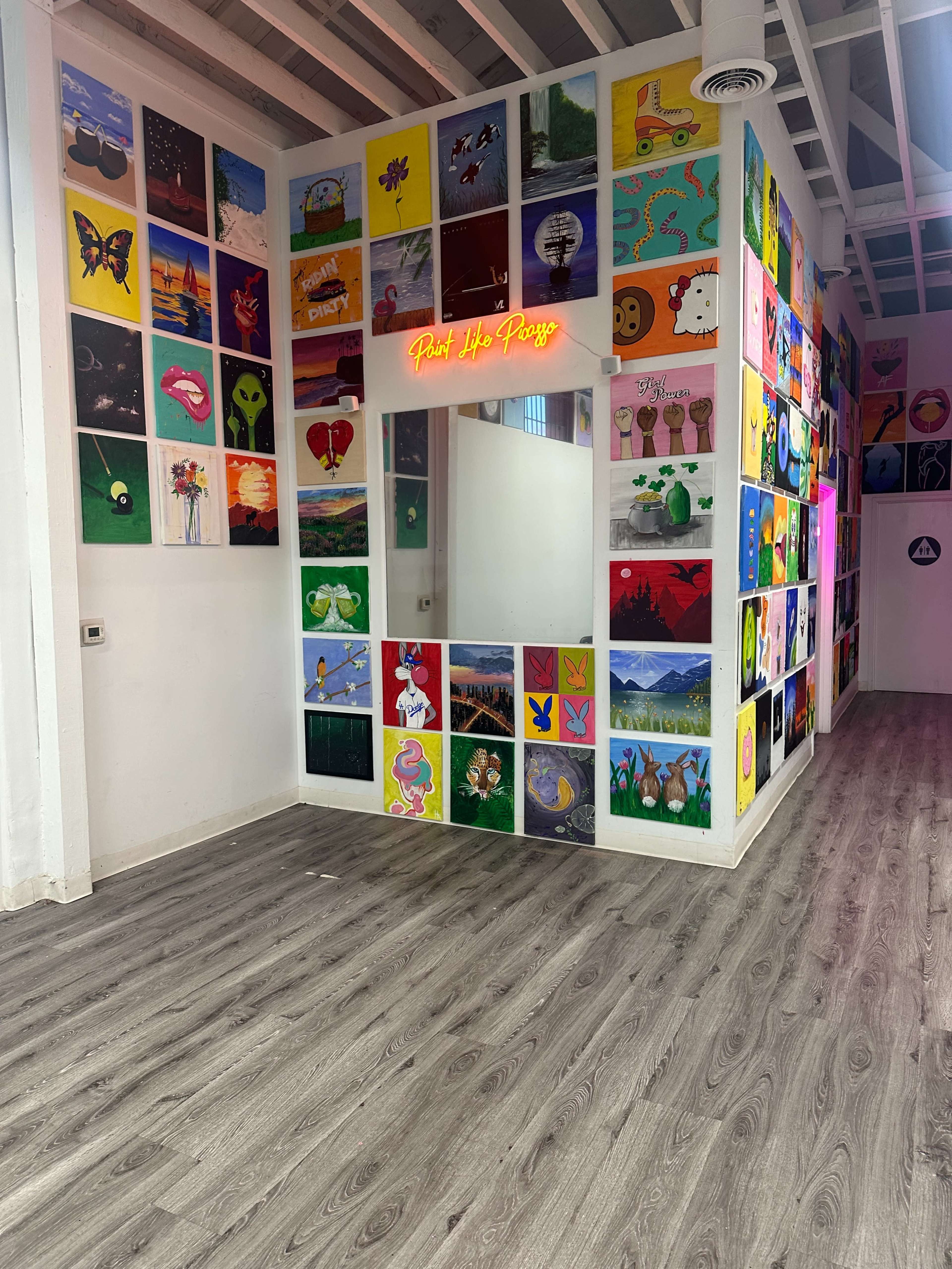 The image shows a gallery-like room with colorful artwork displayed on the walls and a mirror with the words "Paint Life Positive" illuminated above it.