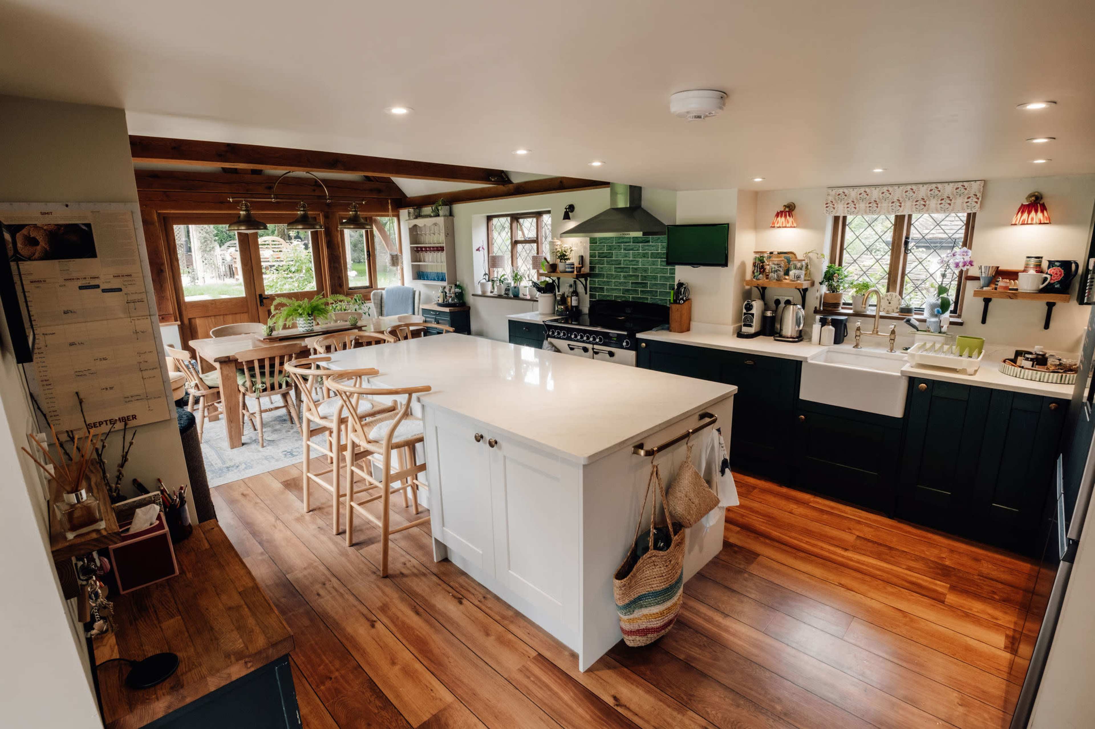 The image shows a spacious kitchen with an island, hardwood flooring, and dining area, featuring modern appliances and green tile accents.