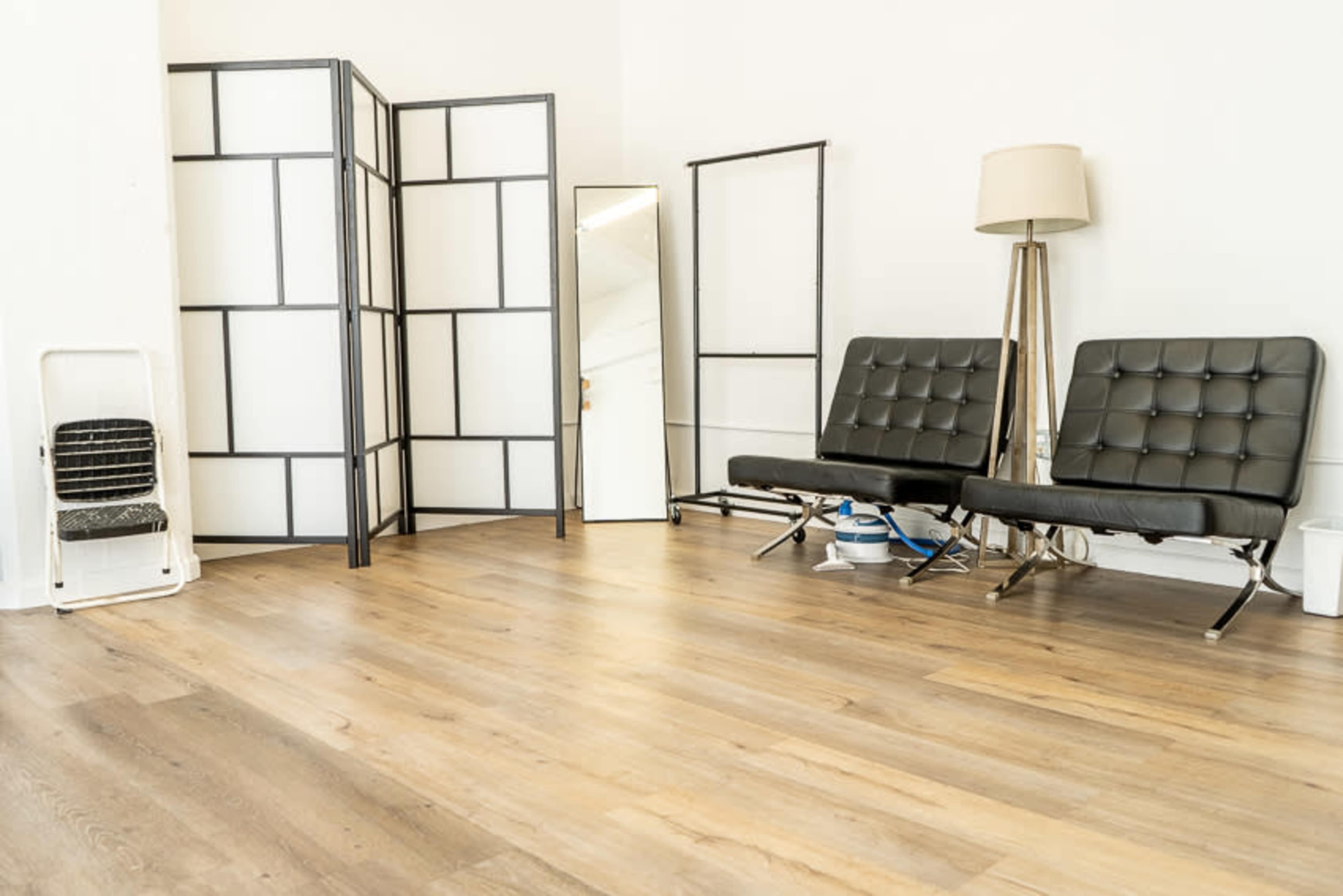A minimalist room with two black chairs, a lamp, a folding screen, a mirror, and light wooden flooring.