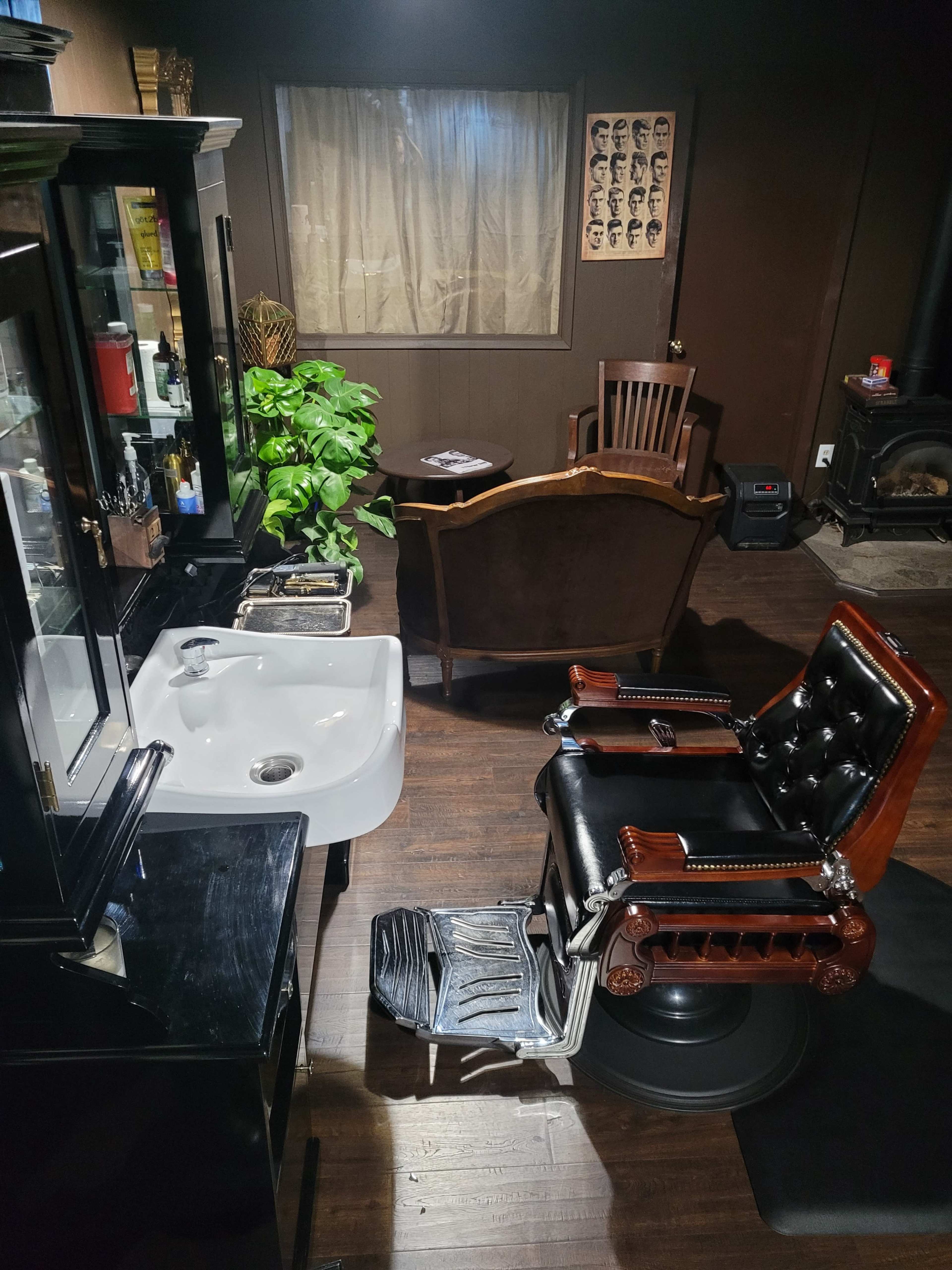 The image shows a vintage-style barber shop interior featuring a black barber chair, a sink, and a waiting area with a wooden chair, illuminated by soft lighting.
