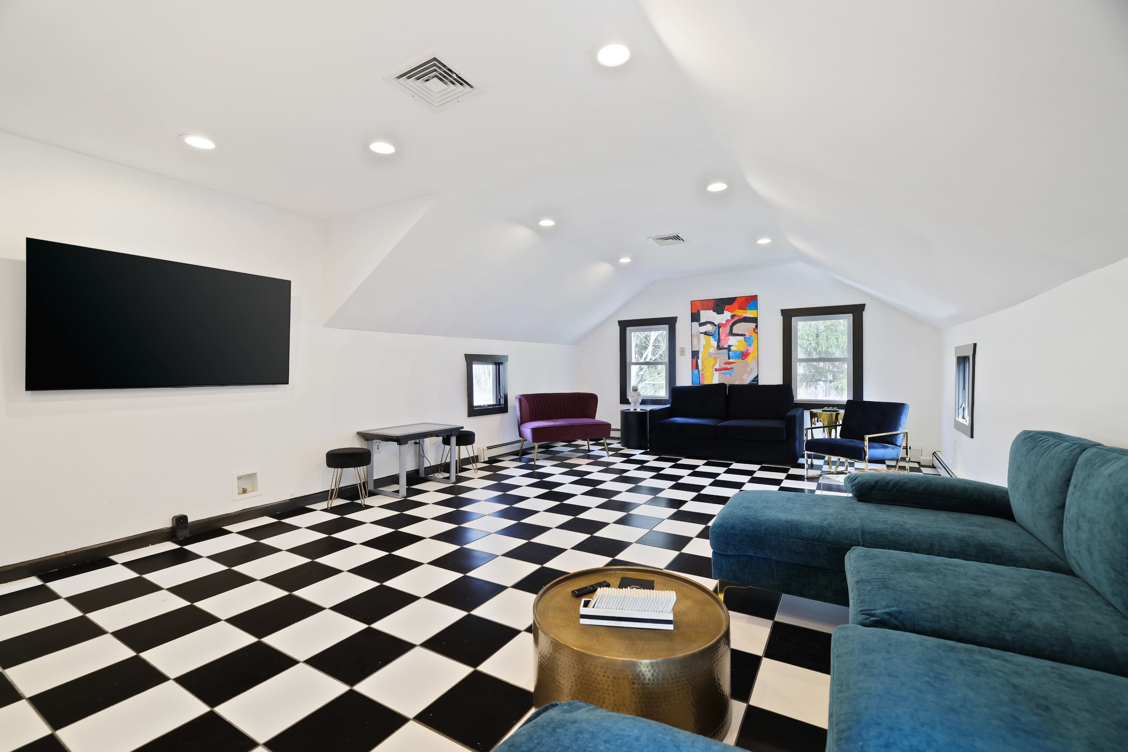 The room features a checkered black and white floor, a large television on the wall, and various seating arrangements, including a blue sectional sofa and two other chairs.