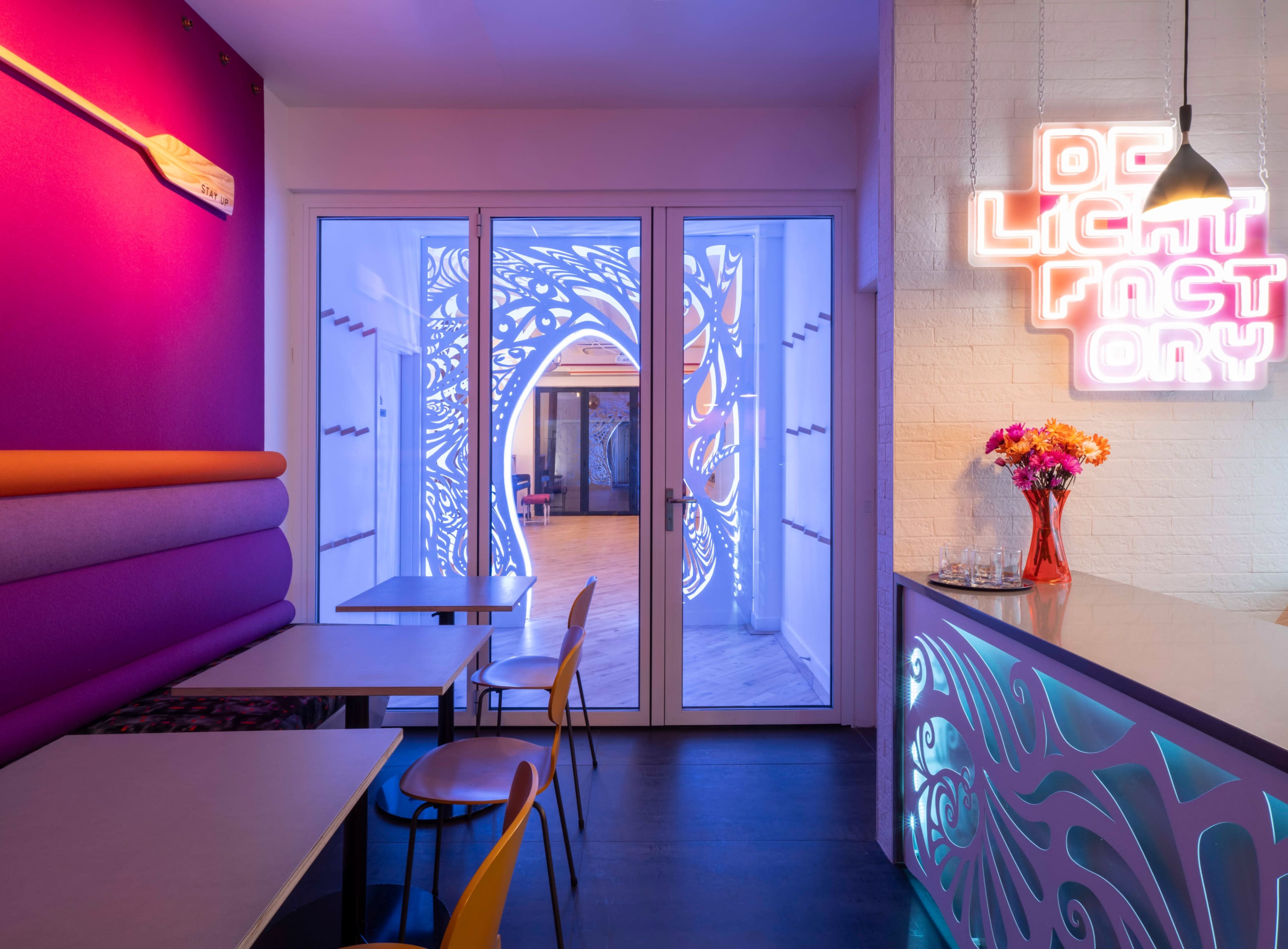The image shows the interior of a modern café with colorful walls and a doorway featuring intricate light designs.