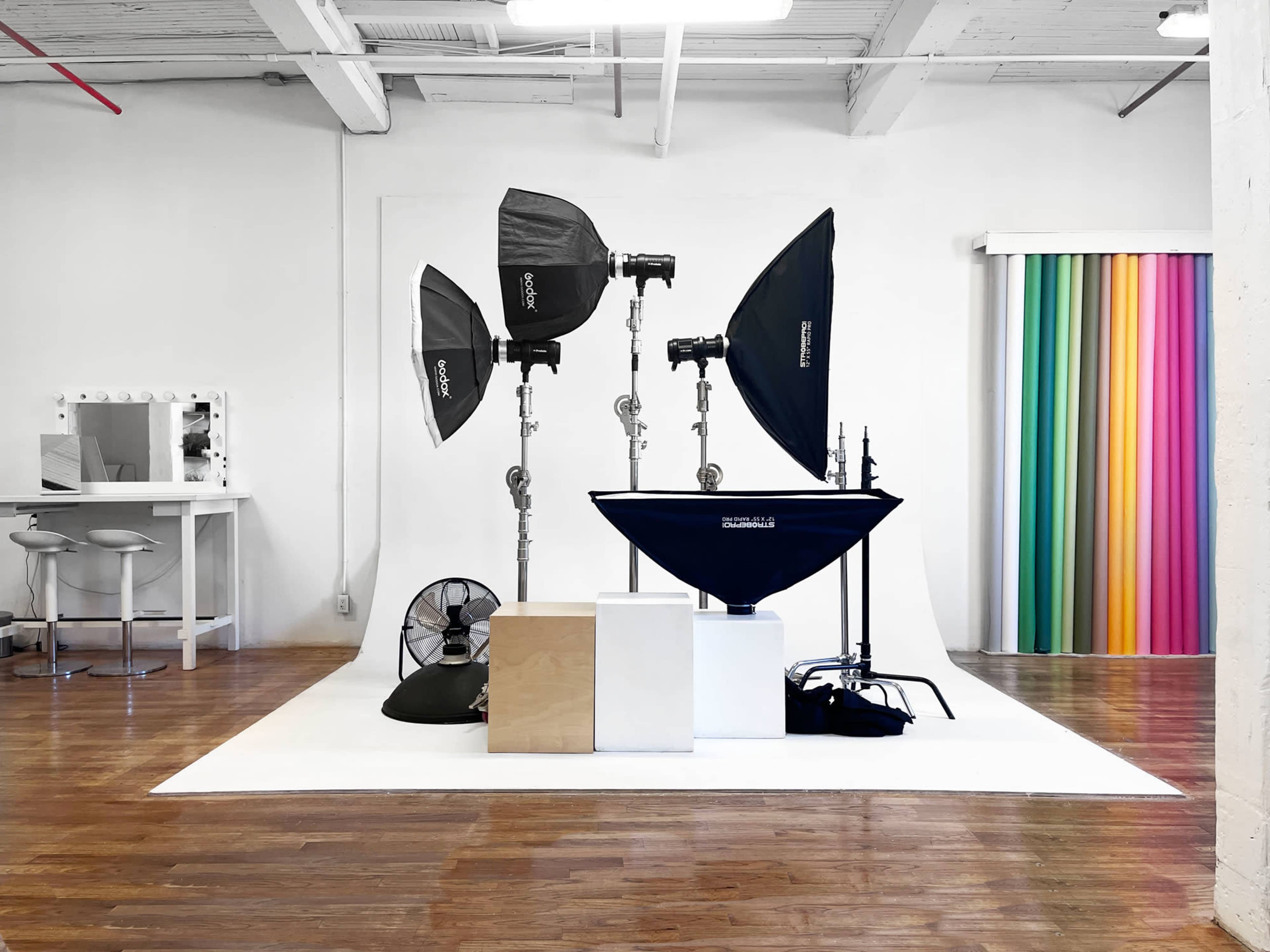 The image shows a photography studio setup with several light modifiers, a fan, and a colorful backdrop.