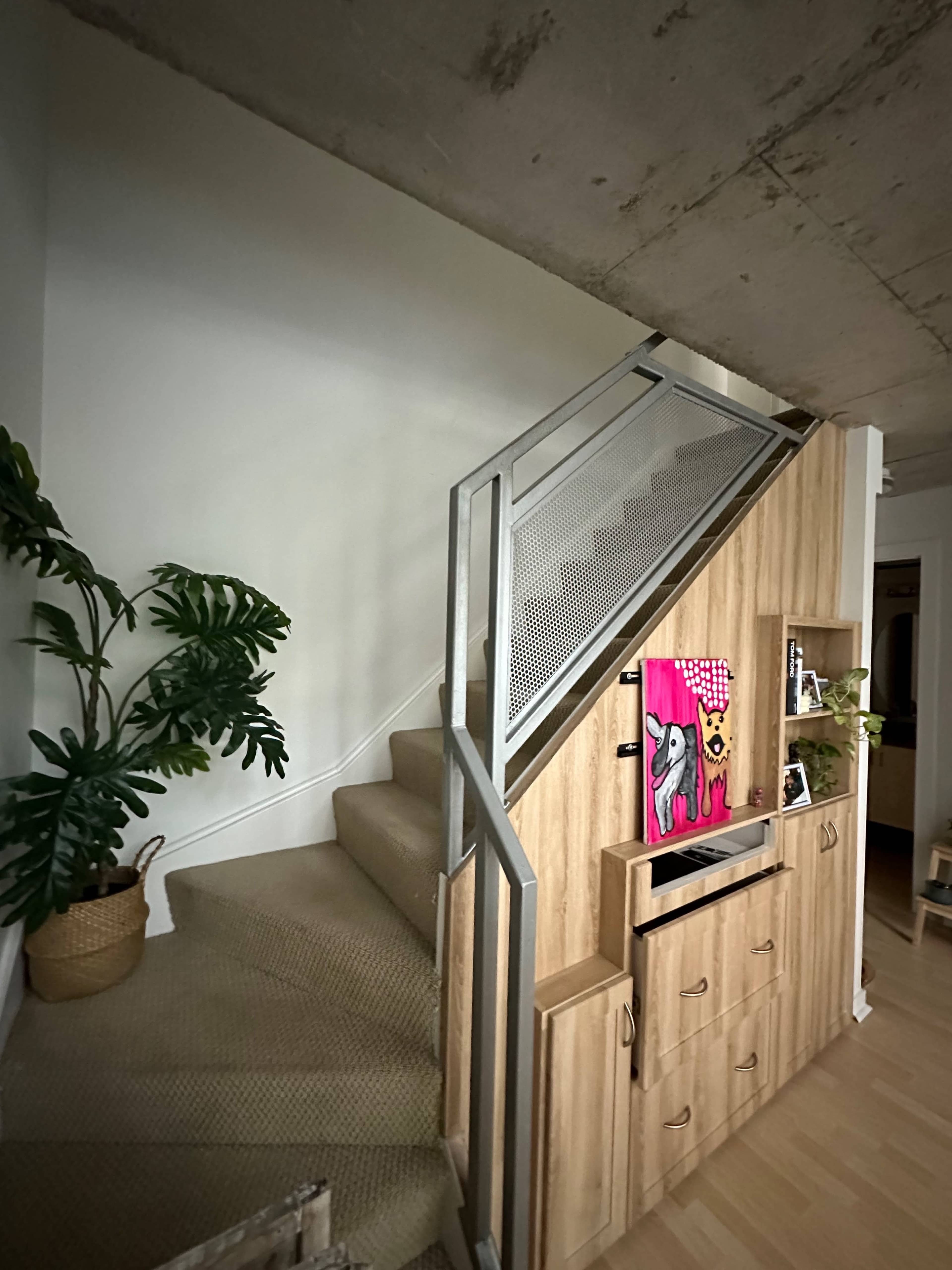 A staircase leads upwards beside a wooden storage unit and a potted plant in a well-lit interior space.